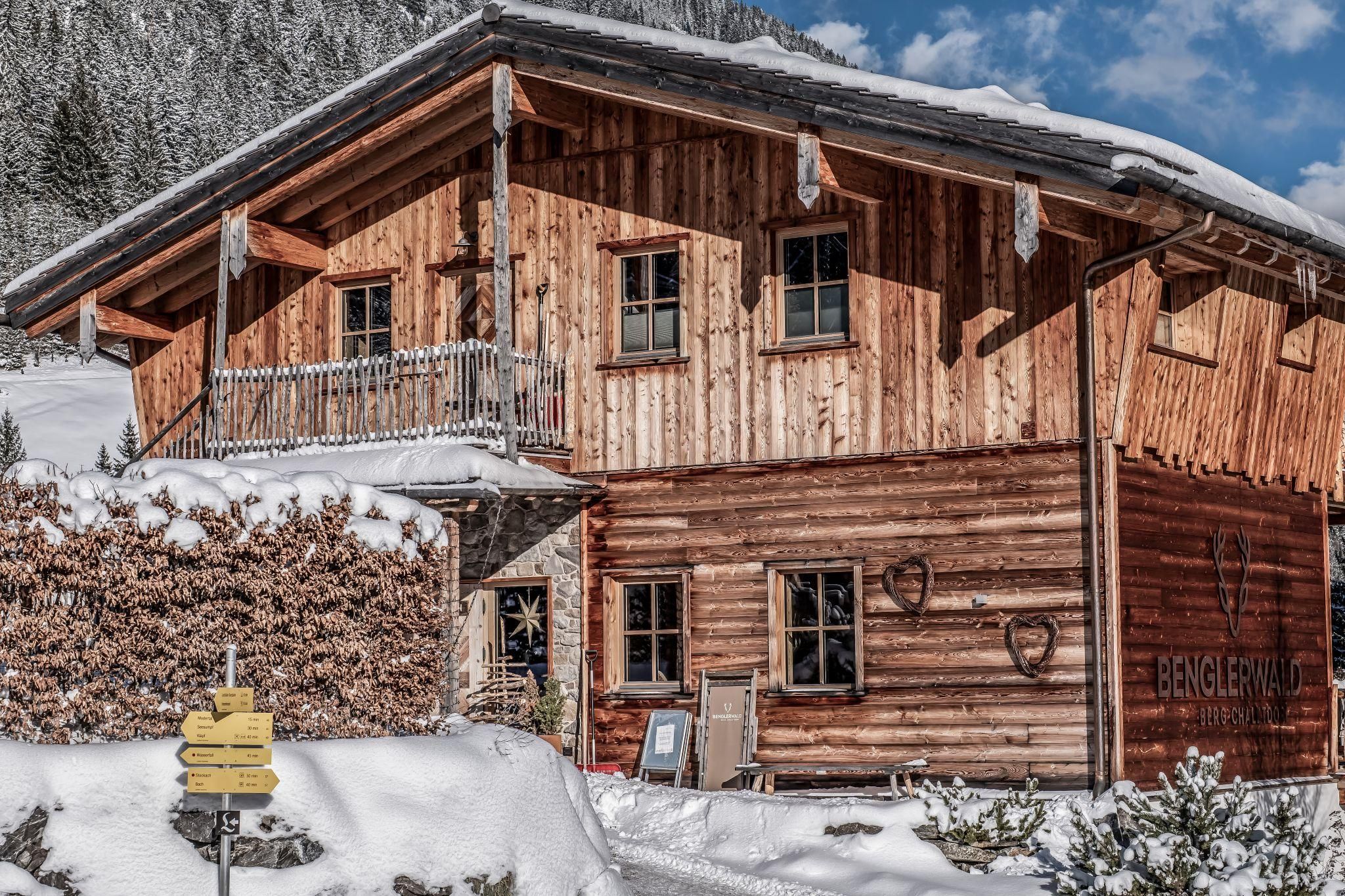 Ein Chalet in den Bergen, umgeben von Schnee. Die Architektur ist rustikal mit einem einladenden Balkon.