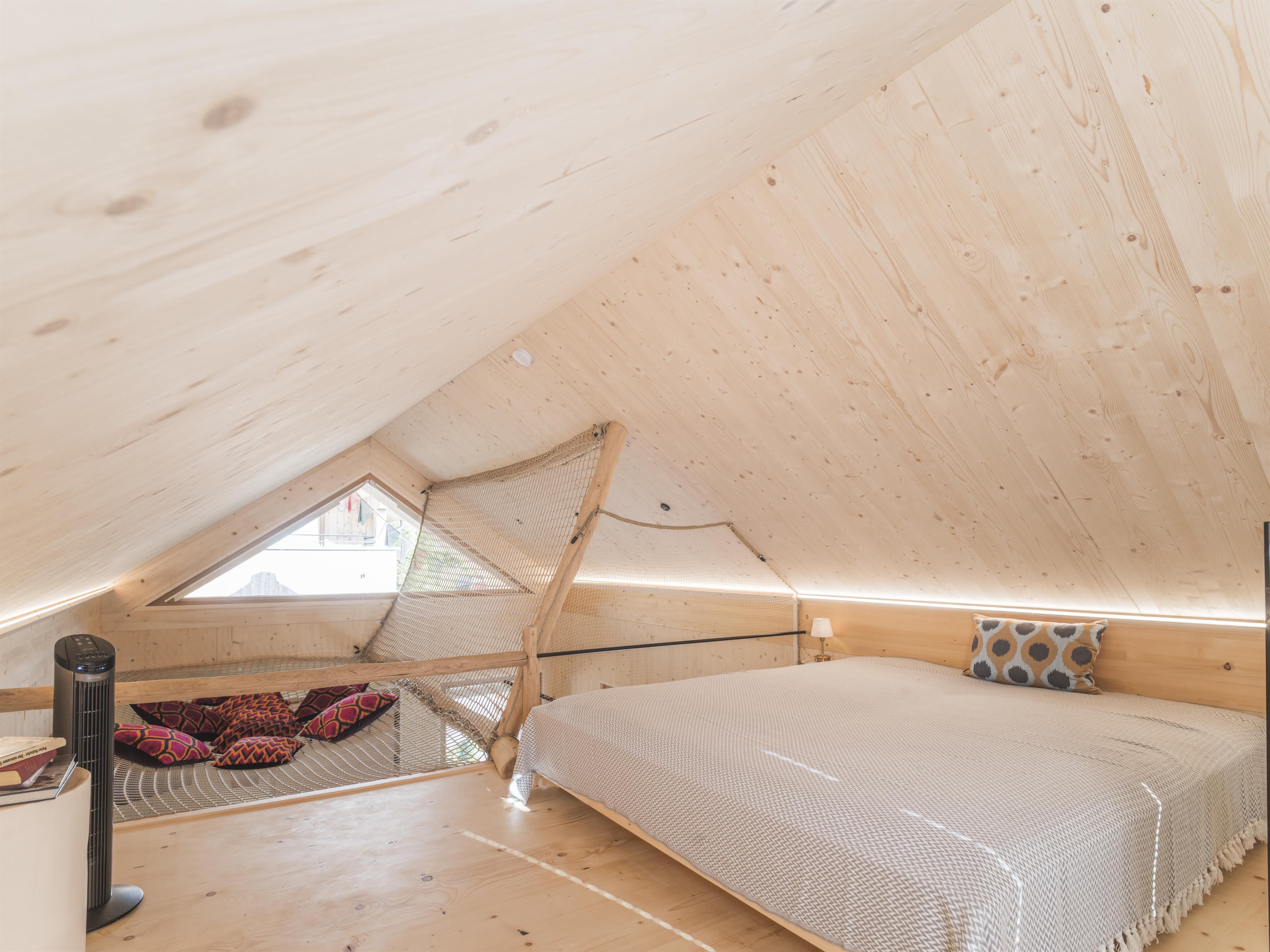 Ein gemütliches Schlafzimmer mit Holzdecke und einer großen Fensteröffnung. Das Zimmer ist hell und modern dekoriert.