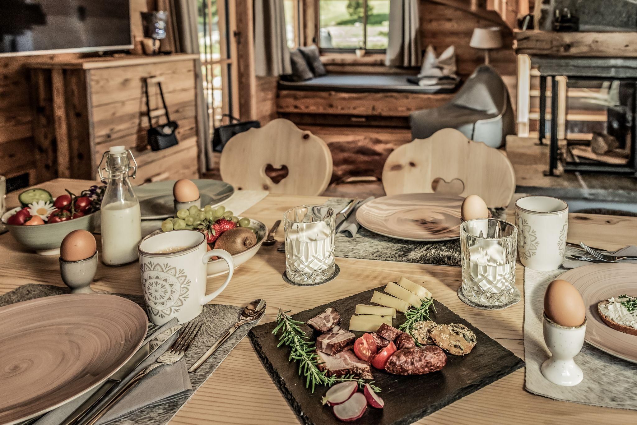 Ein rustikaler Tisch mit einer Vielzahl von Speisen, einschließlich Wurst, Käse und frischem Gemüse. Im Hintergrund ist eine gemütliche, holzverzierte Umgebung sichtbar.