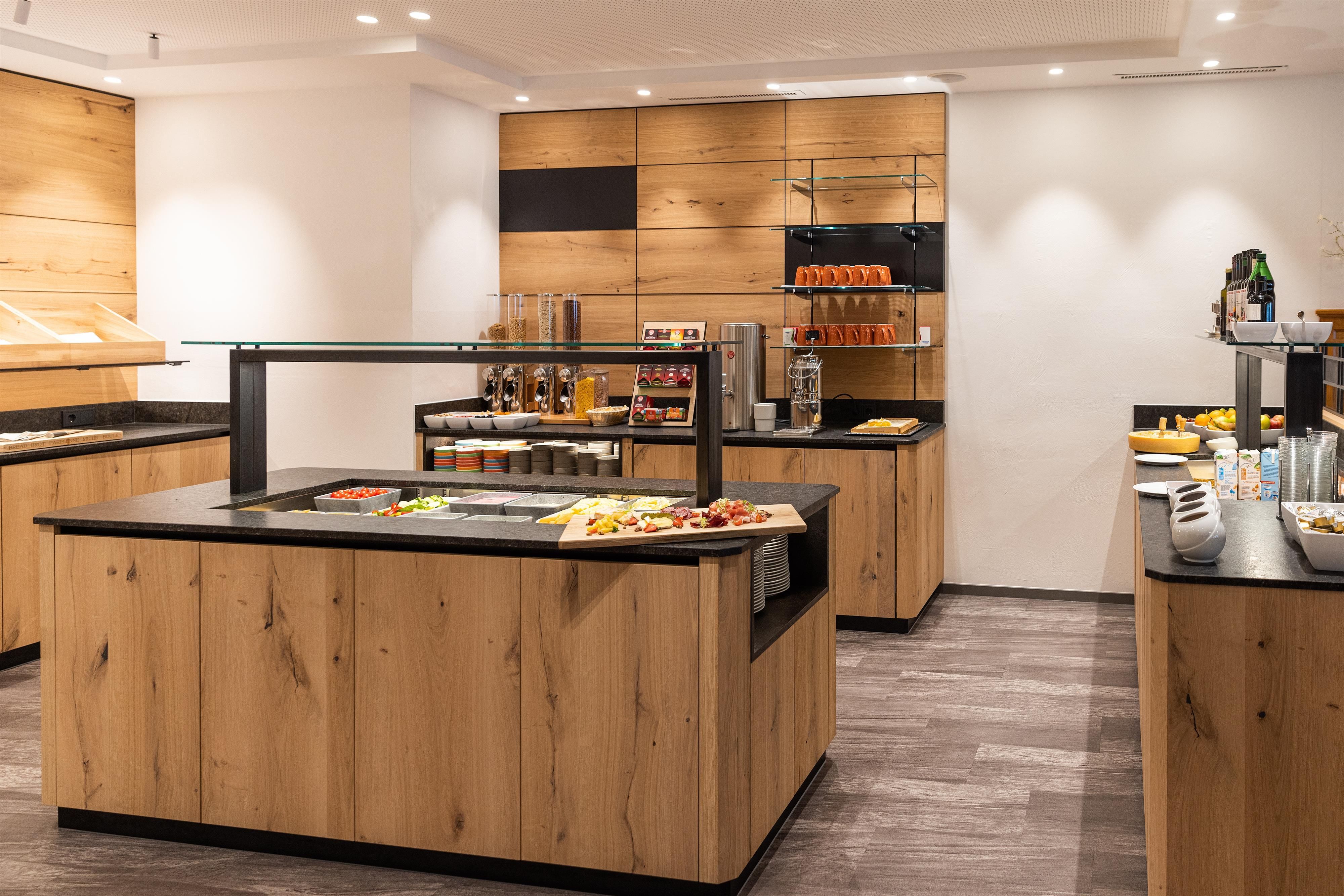 Ein modernes Frühstücksbuffet mit Holzregalen und verschiedenen Speisen. Die hellen Wände und das stilvolle Design schaffen eine einladende Atmosphäre.
