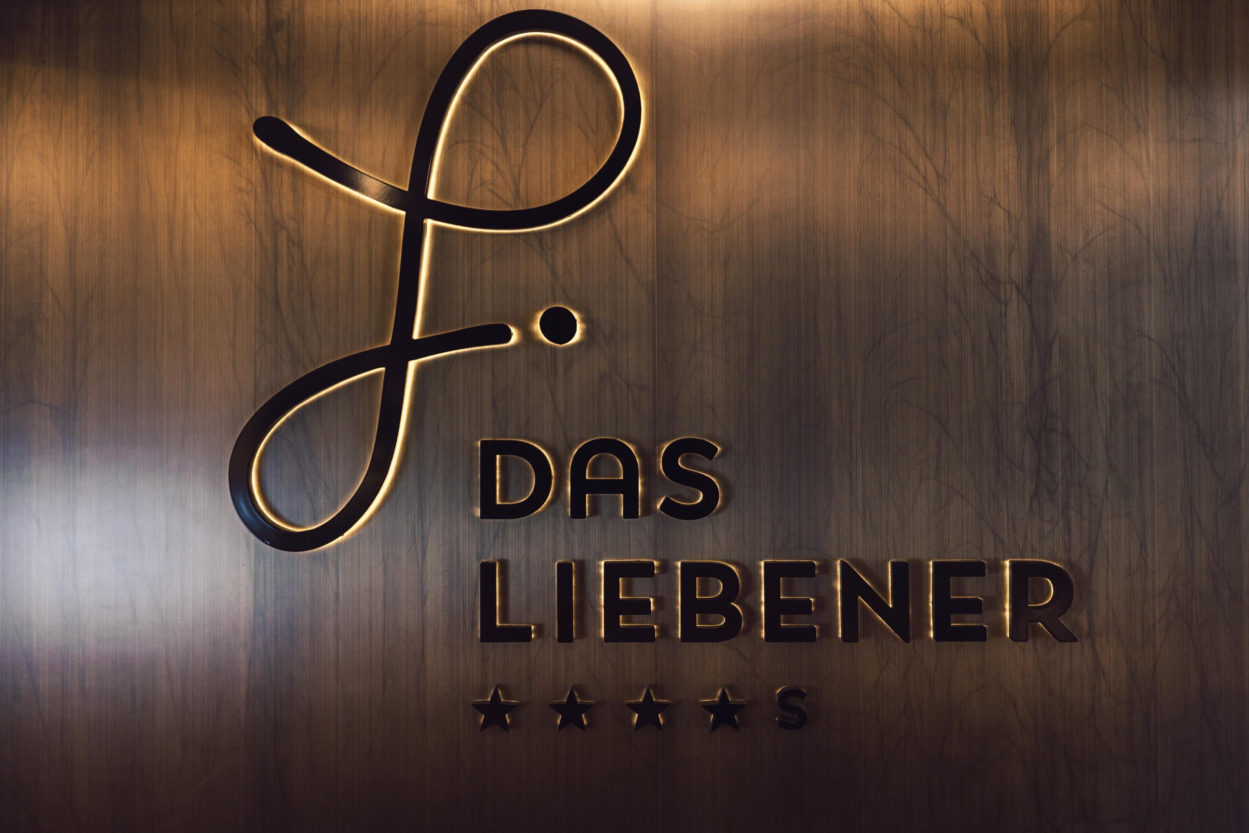 Ein elegantes Schild mit dem Schriftzug „Das Liebener“ und einer geschwungenen Linie. Das Design ist modern und ansprechend auf einem Holzgrund.