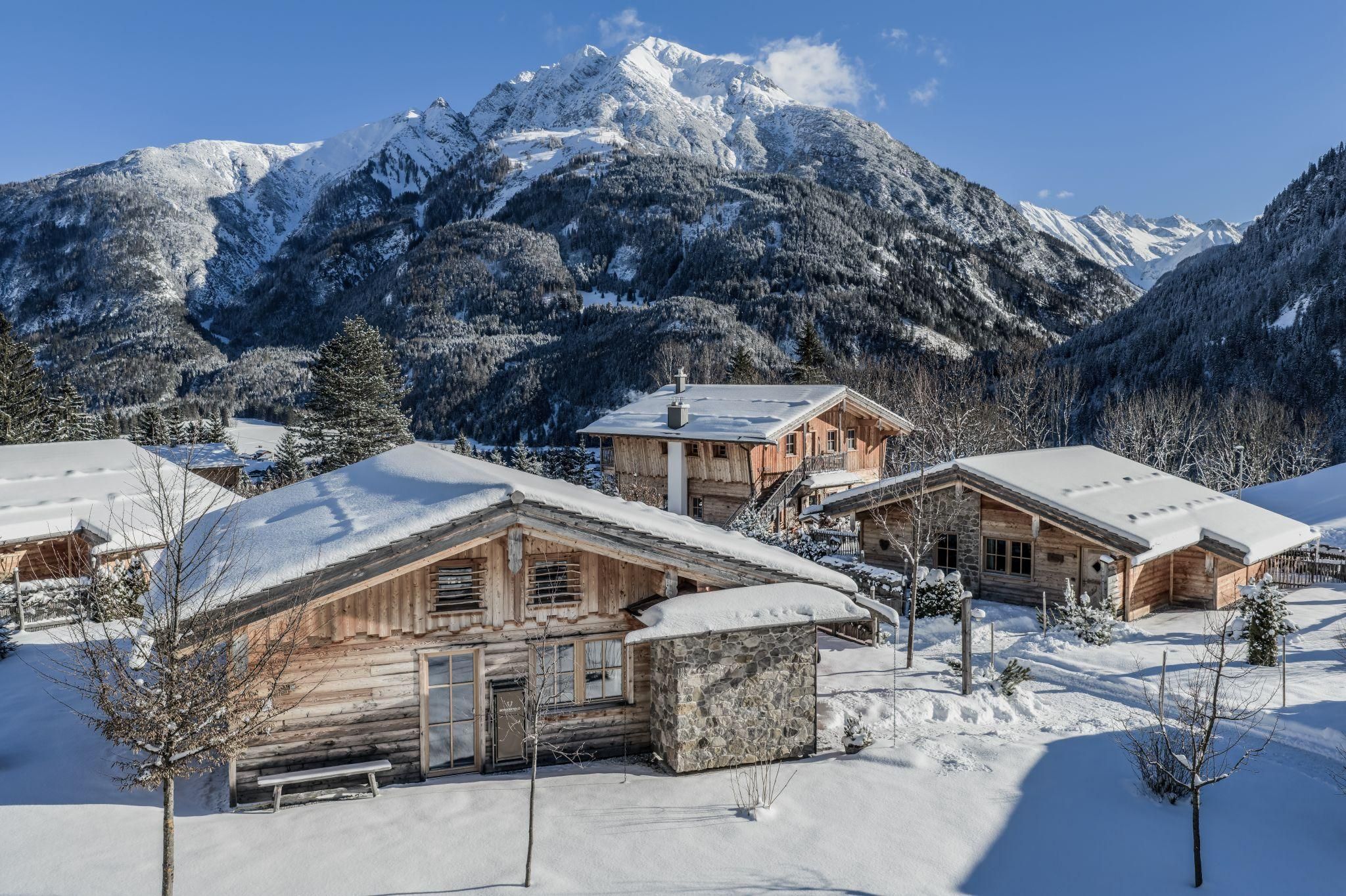 Eine verschneite Berglandschaft mit Holzchalets. Die majestätischen Berge erheben sich im Hintergrund unter einem klaren blauen Himmel.