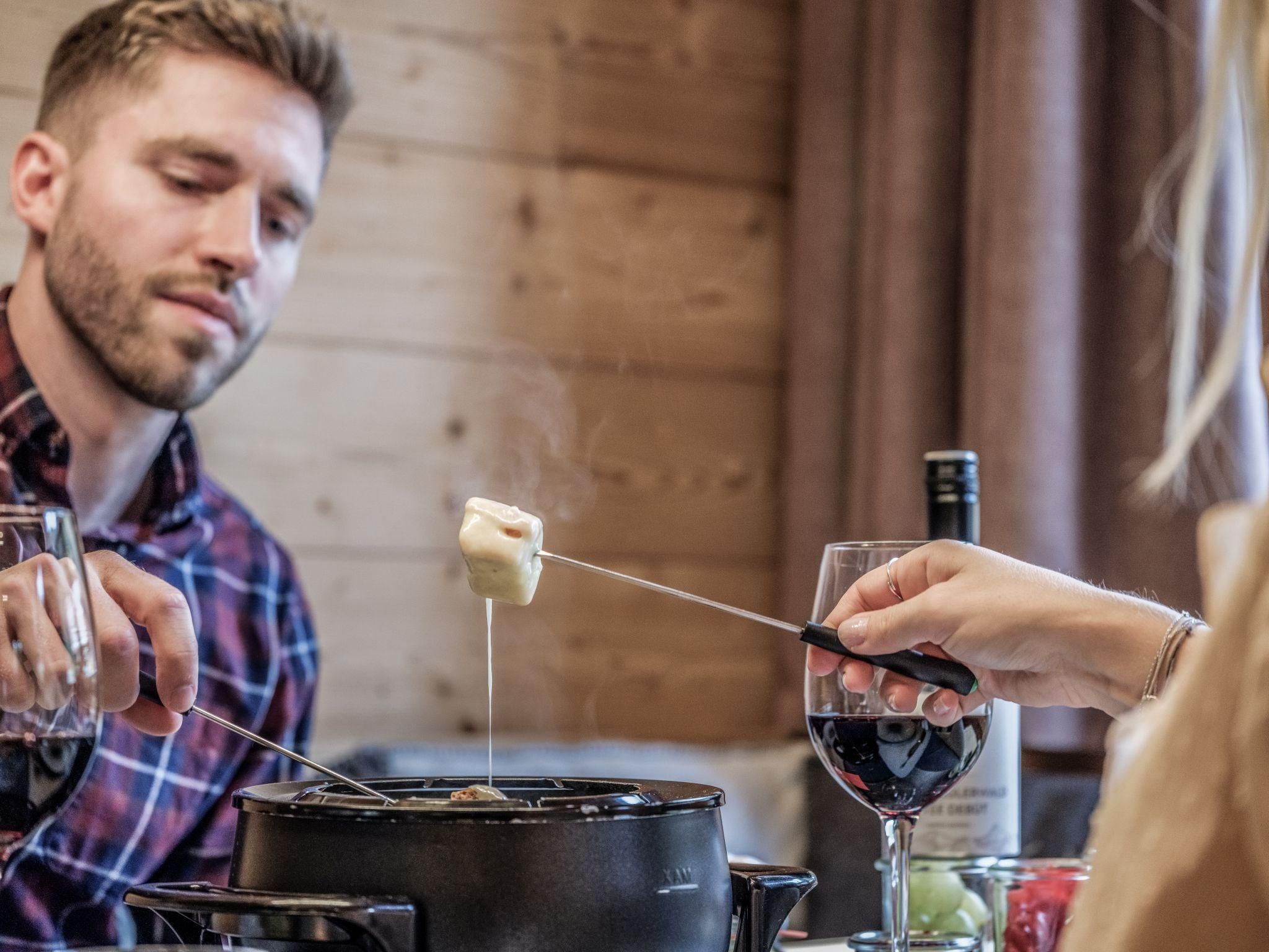 Ein Paar genießt ein Fondue-Essen in einem gemütlichen Ambiente. Rotwein und frisches Gemüse sind ebenfalls auf dem Tisch zu sehen.