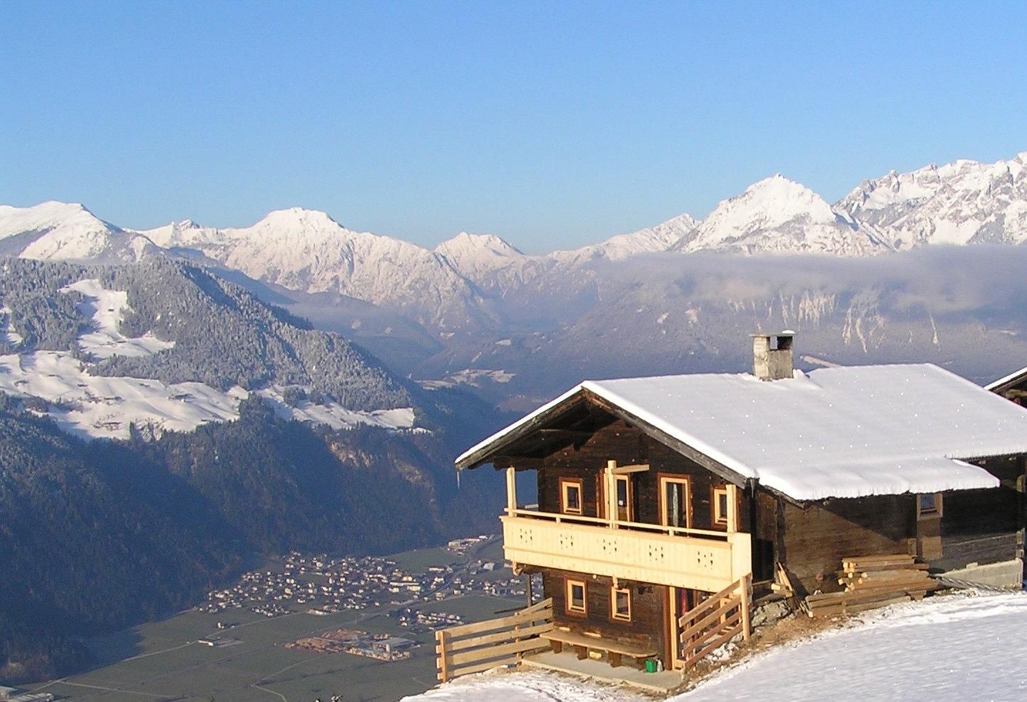 Eine malerische Berghütte in den verschneiten Alpen. Im Hintergrund erheben sich majestätische Berge unter einem klaren blauen Himmel.