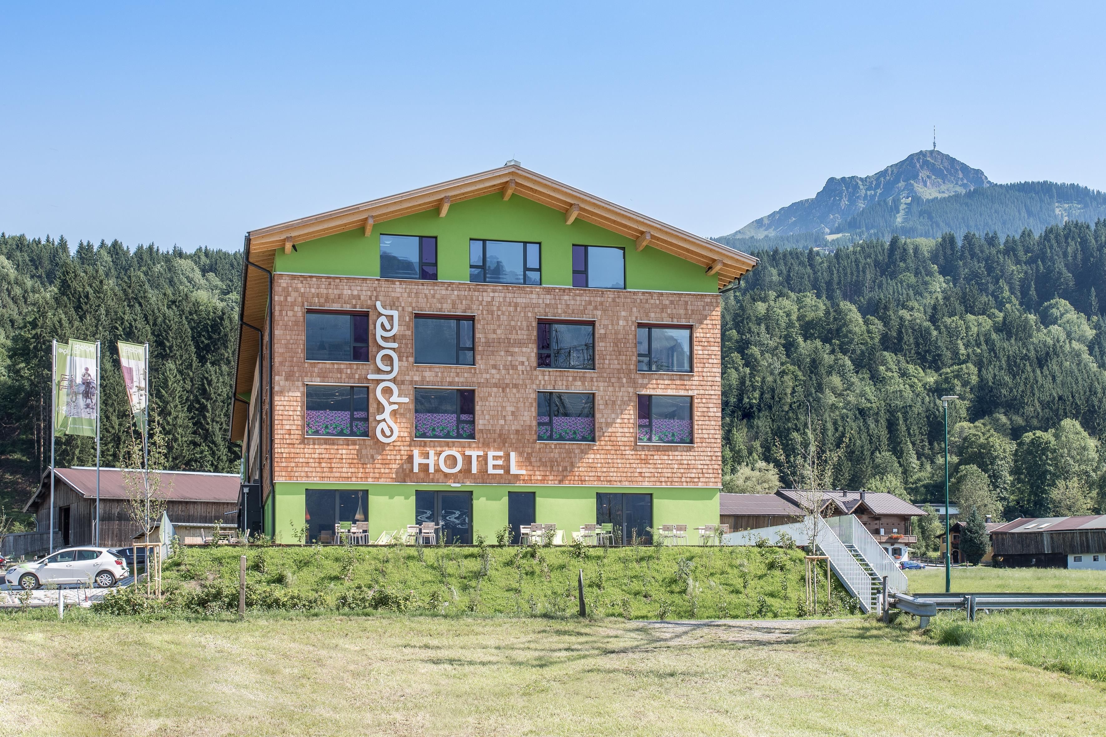 Ein modernes Hotelgebäude mit einem bunten Design und großen Fenstern. Im Hintergrund sind Wälder und Berge zu sehen, die eine schöne Naturkulisse bieten.