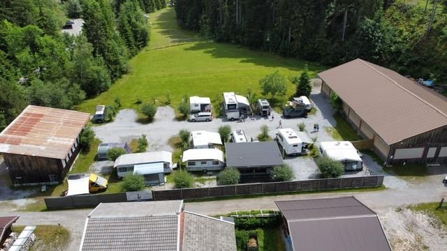 Ein Campingplatz mit mehreren Wohnmobilen und Wohnwagen in einer malerischen Umgebung. Im Hintergrund sind grüne Wiesen und Bäume zu sehen.