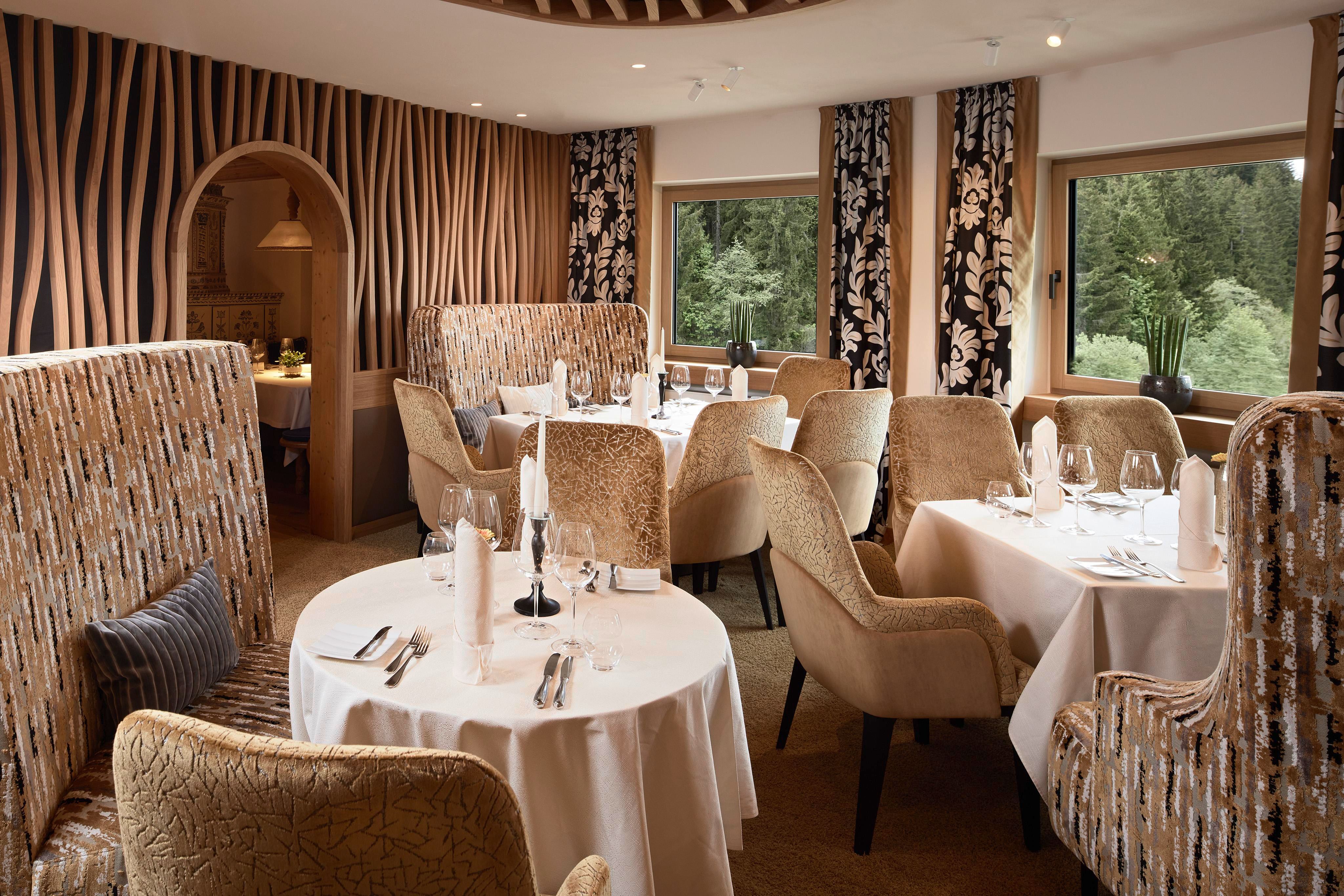 Ein elegantes Restaurant mit stilvollen Sitzgelegenheiten und geschmackvoller Dekoration. Große Fenster bieten einen Blick ins Grüne.
