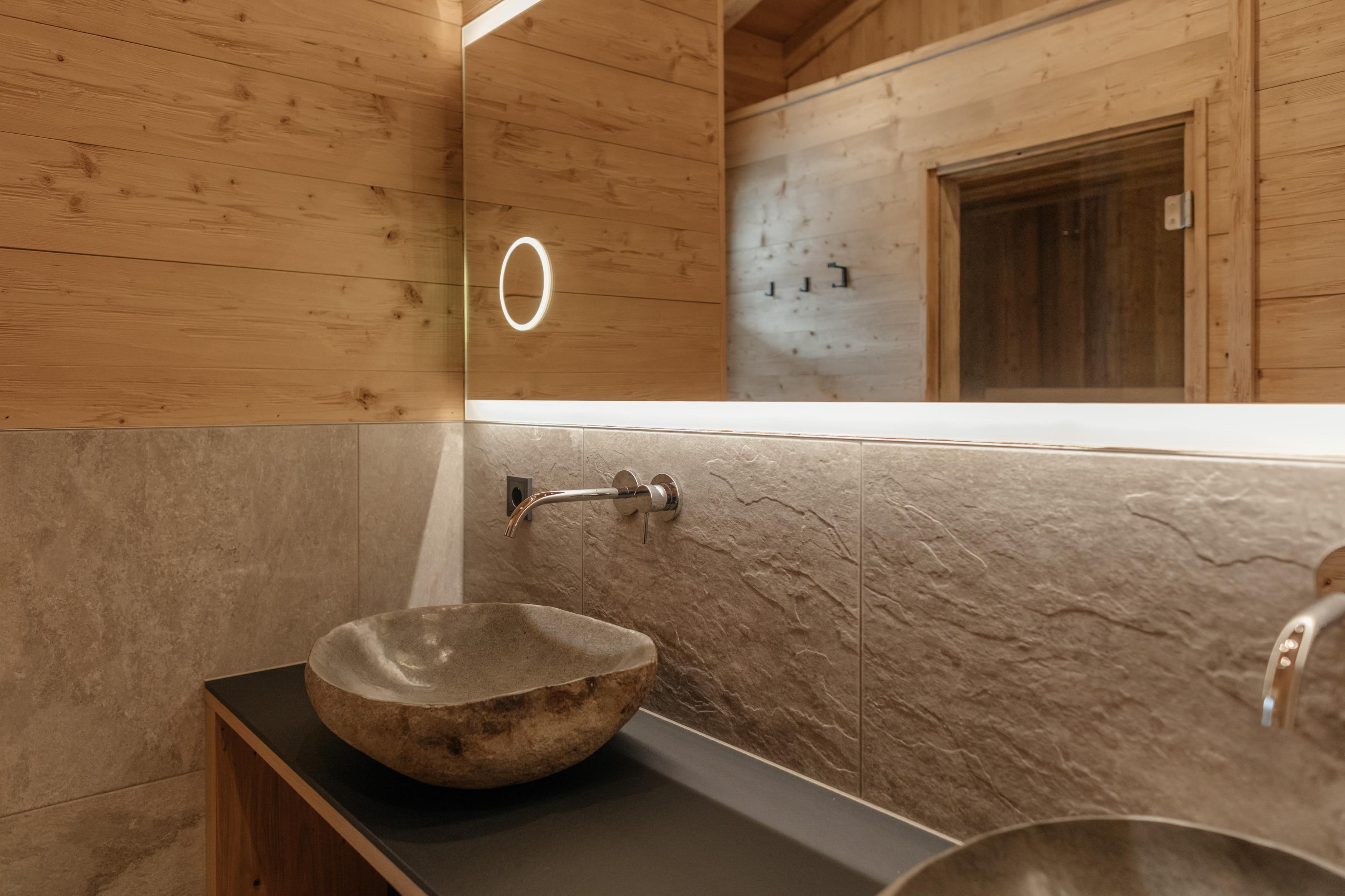 Ein modernes Badezimmer mit einer eleganten Steinschüssel und Holzverkleidung. Die sanfte Beleuchtung sorgt für eine warme Atmosphäre.