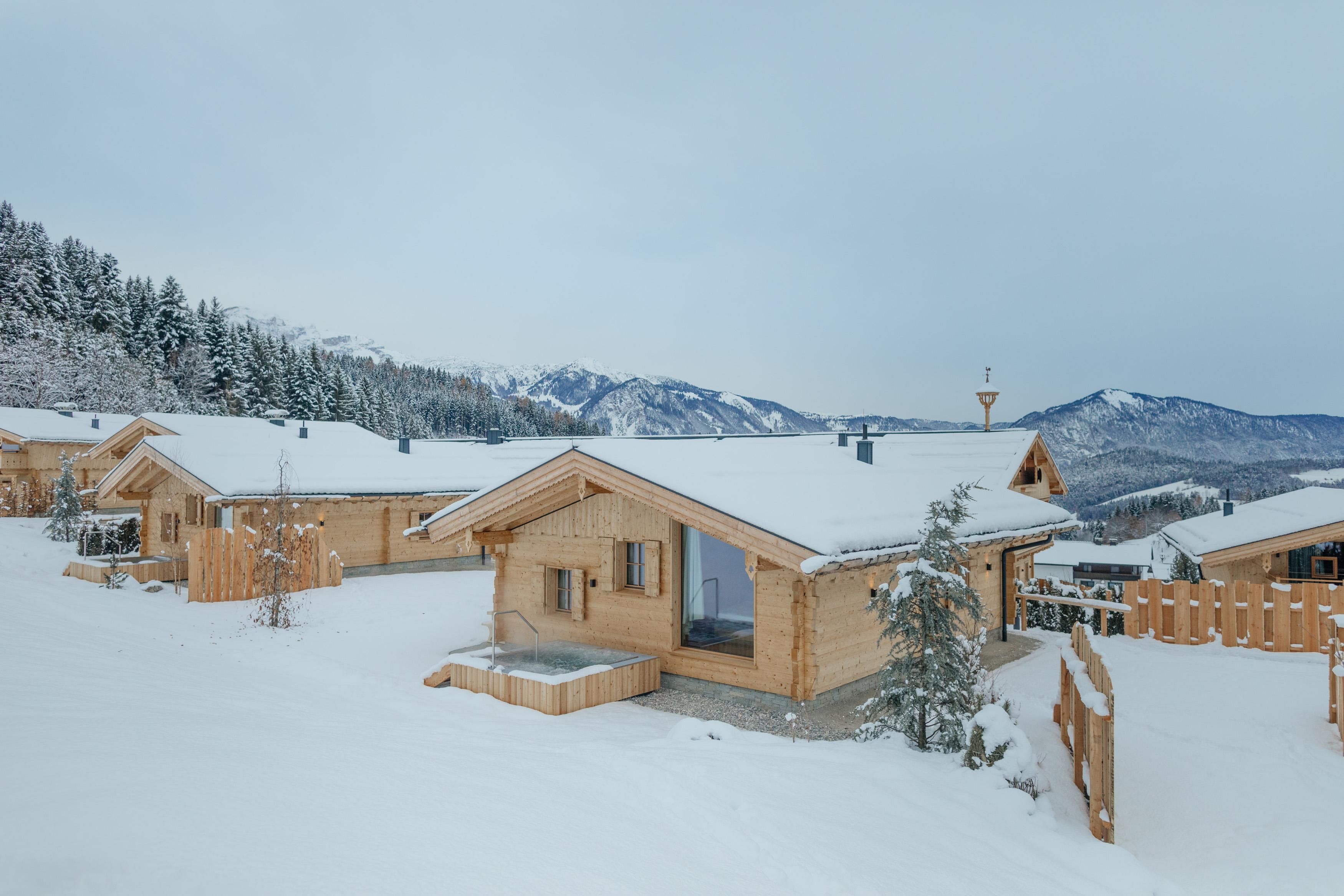 Eine gemütliche Chalet-Landschaft im Schnee, umgeben von Bergen. Die Hütten sind aus Holz und harmonieren mit der winterlichen Umgebung.