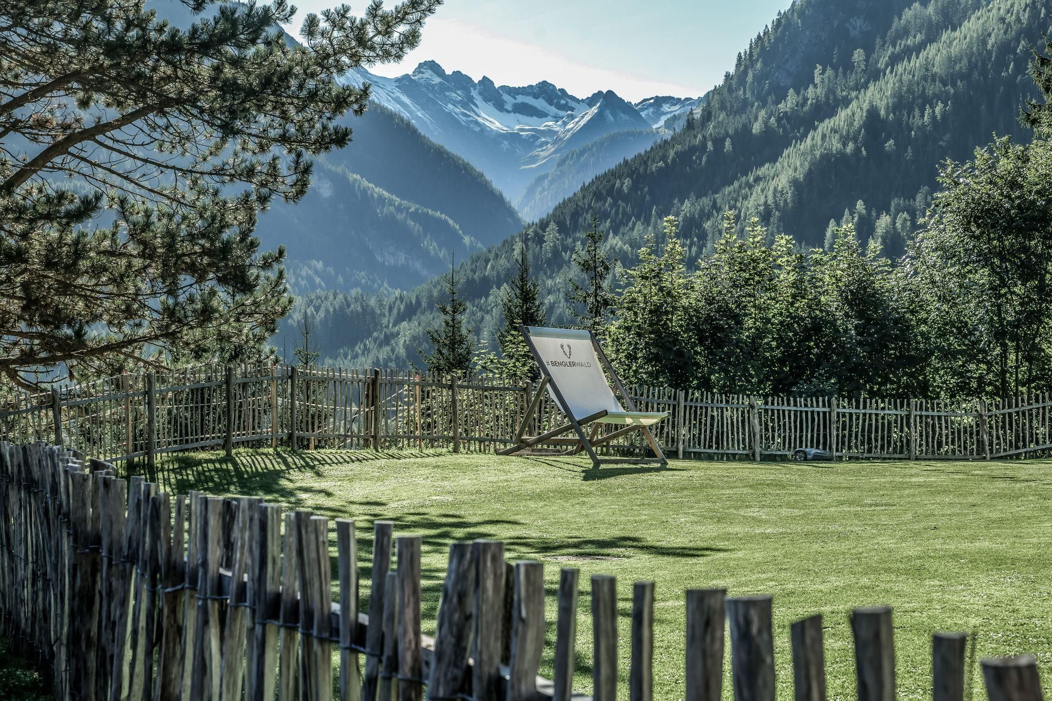Eine ruhige Berglandschaft mit grünen Wiesen und majestätischen Bergen im Hintergrund. Ein bequemer Liegestuhl steht in der Mitte der Szenerie.