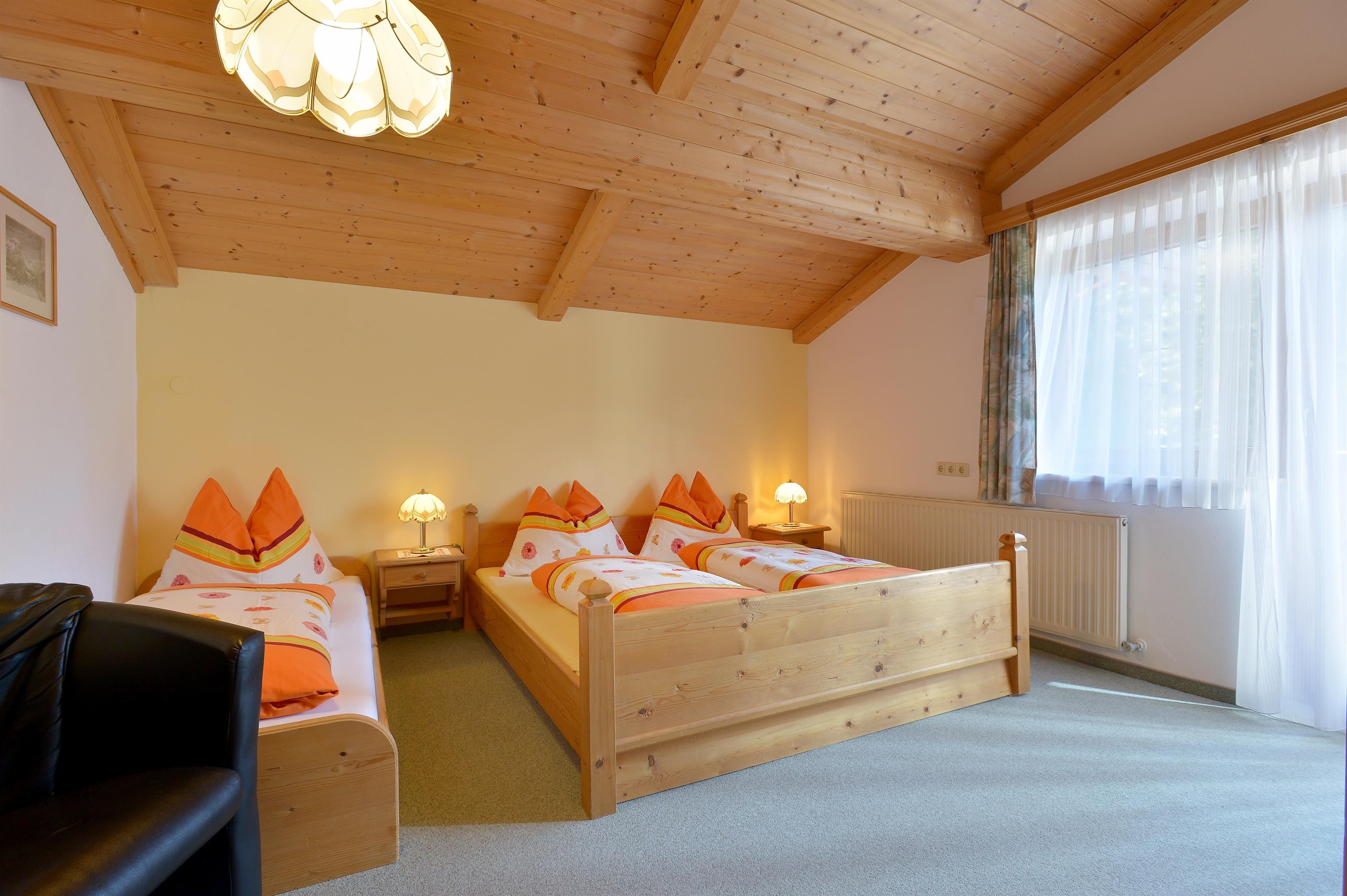 Ein gemütliches Schlafzimmer mit drei Betten aus Holz und einer warmen Holzdecke. Die Fenster lassen viel Licht herein und sorgen für eine angenehme Atmosphäre.