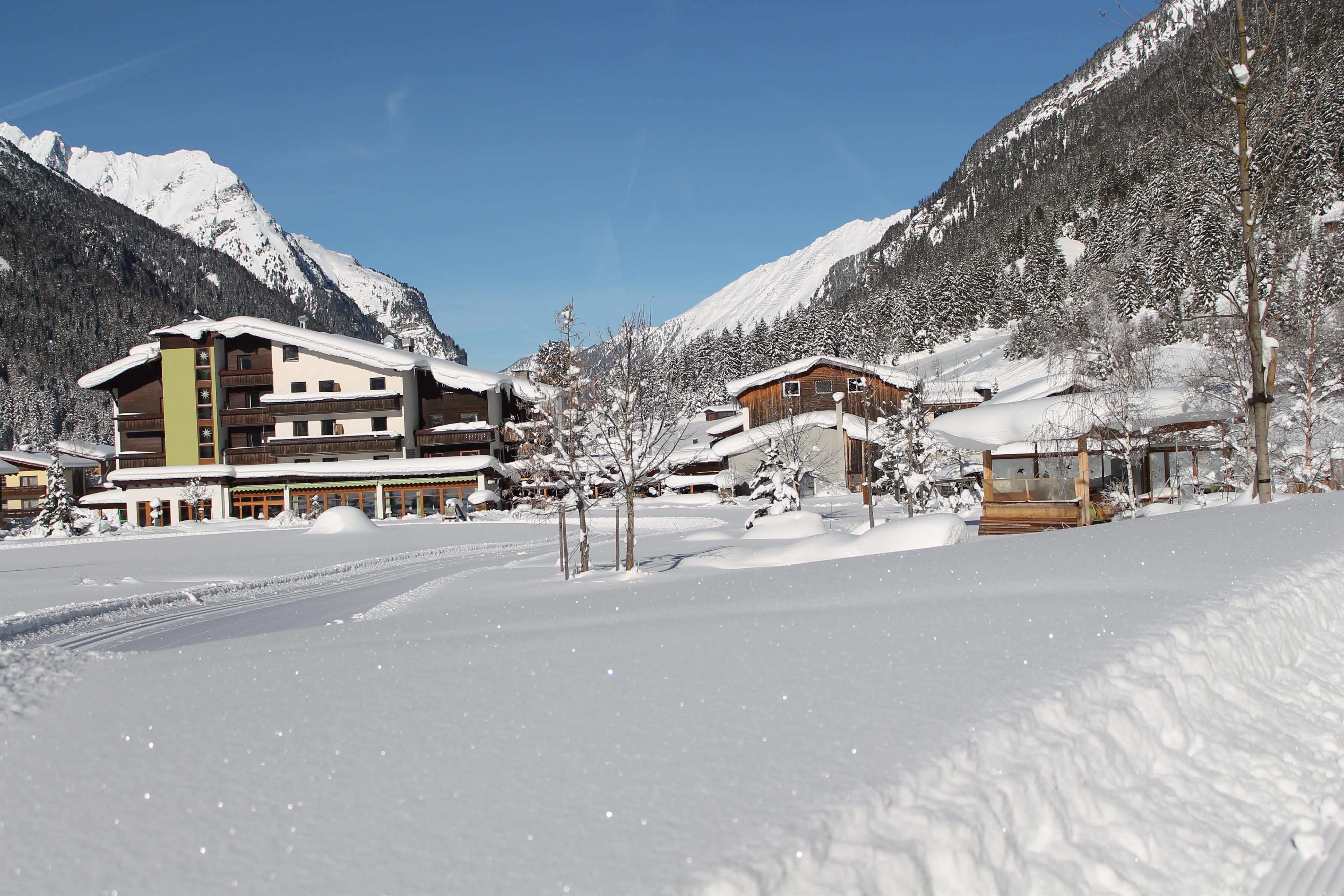 Eine verschneite Landschaft mit einem Hotel und Bergen im Hintergrund. Der Himmel ist klar und blau.