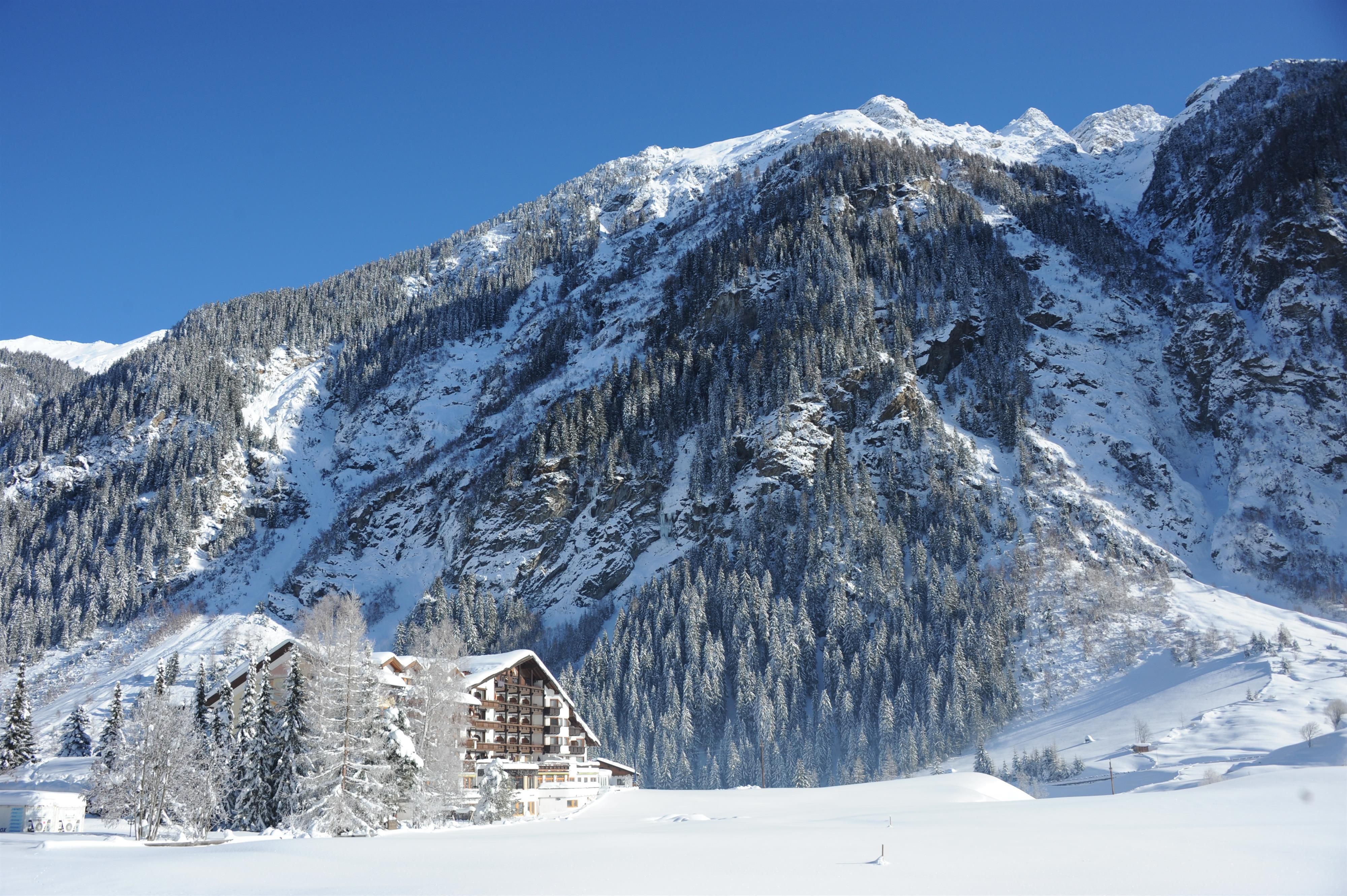 Eine winterliche Landschaft mit schneebedeckten Bergen und einem gemütlichen Hotel. Der klare blaue Himmel ergänzt die friedliche Atmosphäre.