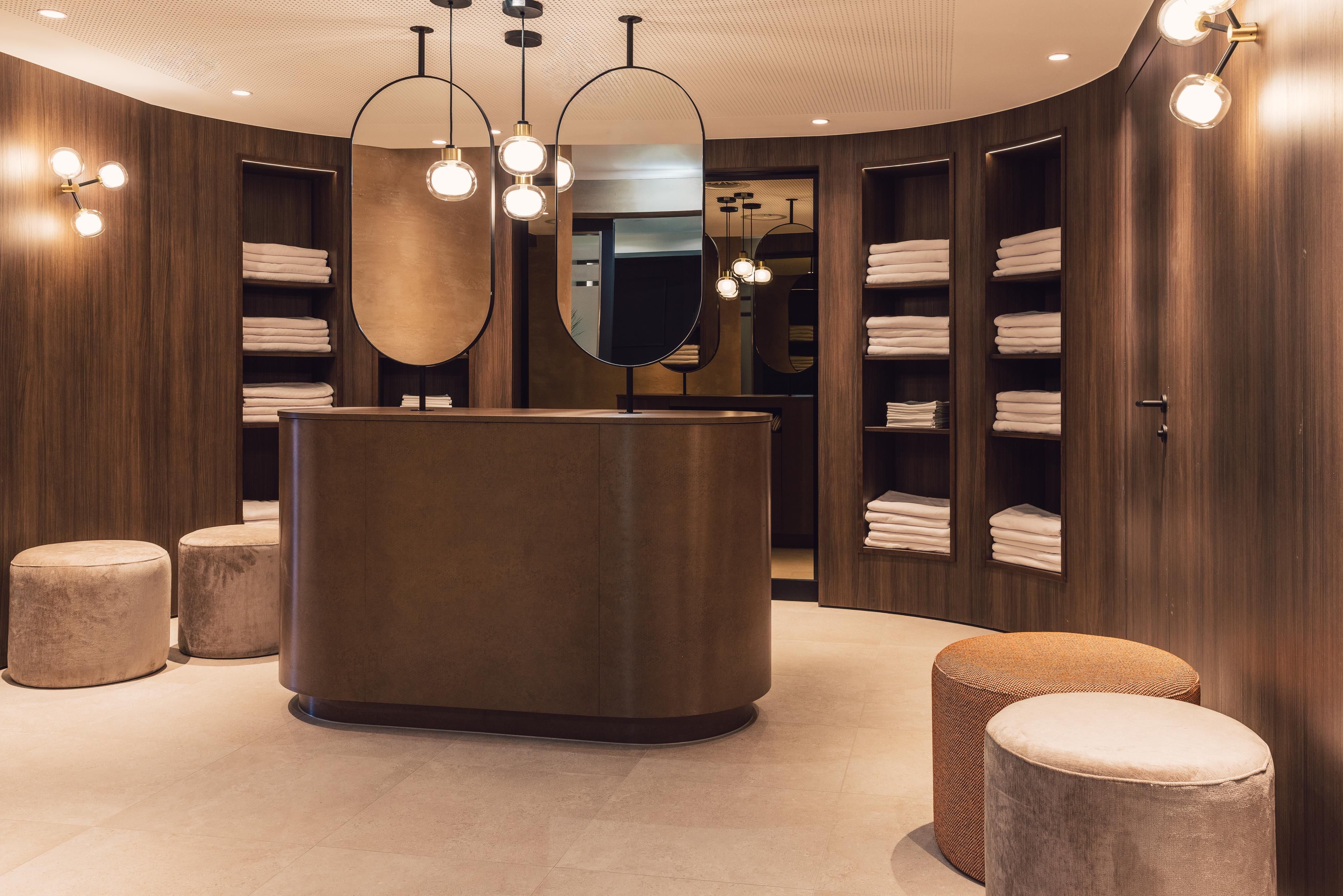 Ein moderner Empfangsbereich mit runden Spiegeln und warmem Holz. Gestapelte Handtücher und stilvolle Sitzgelegenheiten schaffen eine einladende Atmosphäre.