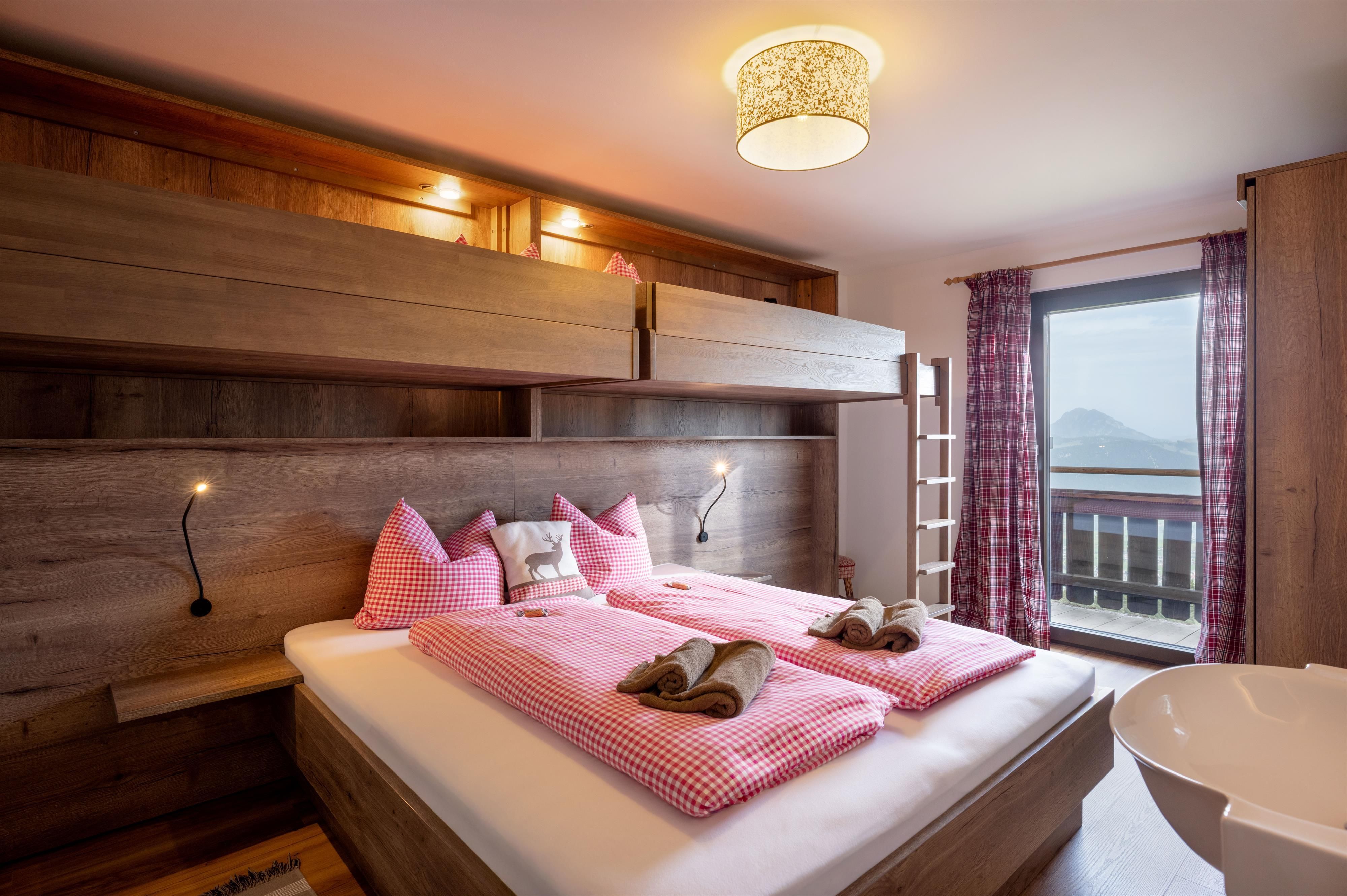 Ein modernes Schlafzimmer mit Holzinterieur und einem großen Fenster. Die Bettwäsche ist in sanften Rosa-Tönen gehalten.