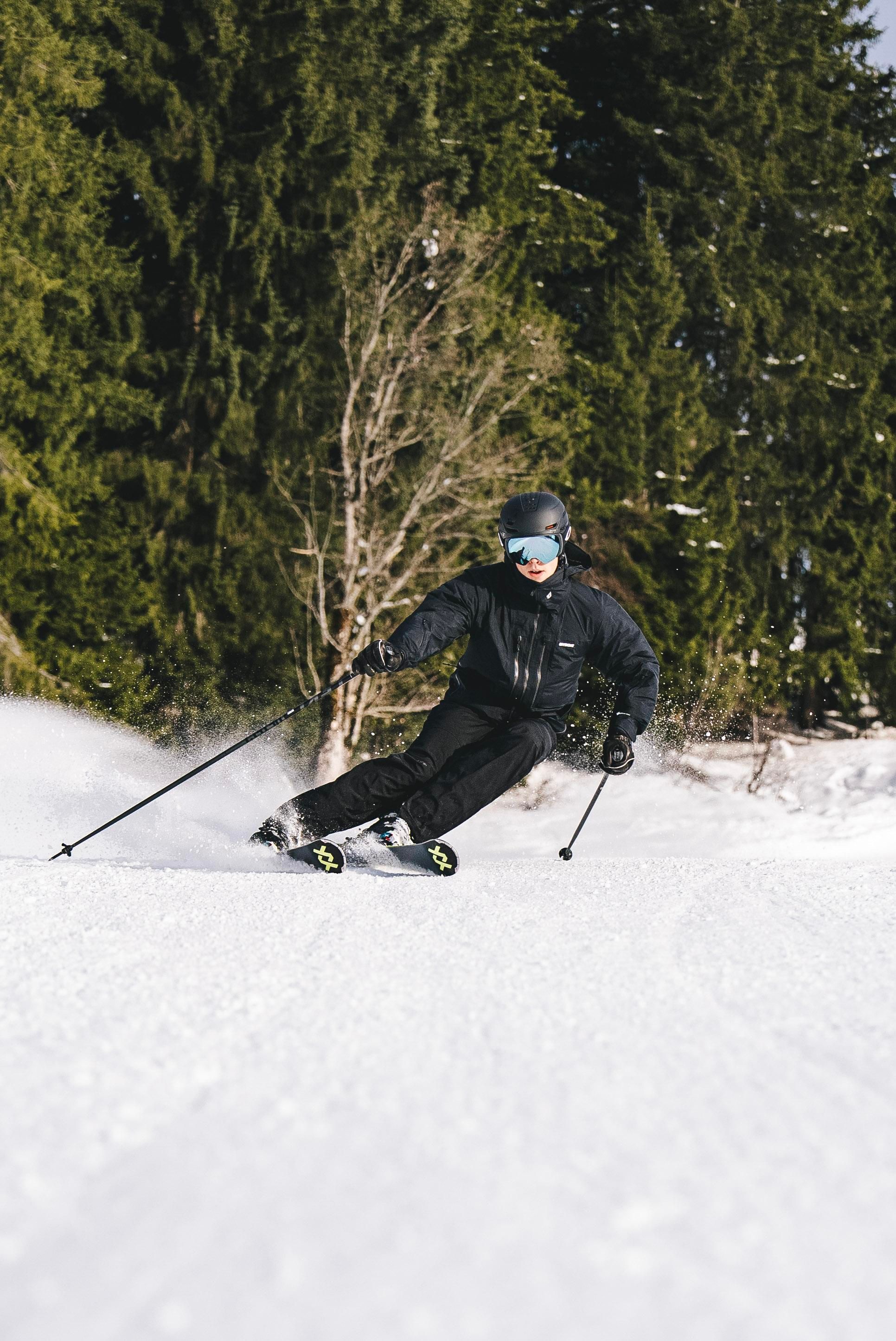 Ein Skifahrer fährt durch den Schnee in einem Wald. Die Umgebung ist winterlich und die Bäume sind grün.