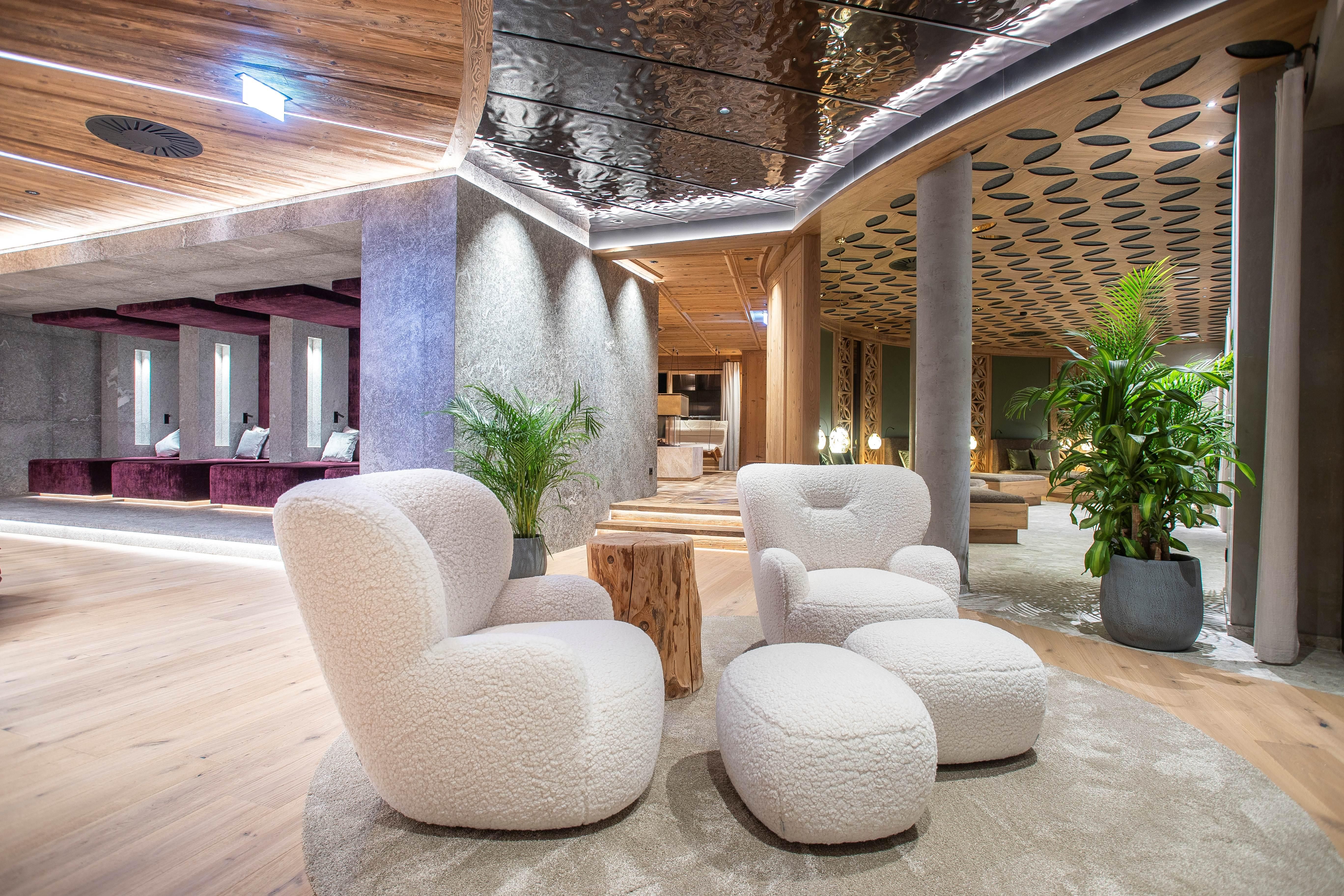 Ein moderner Empfangsbereich mit bequemen, weißen Sesseln und einem kleinen Tisch. Grüne Pflanzen und sanfte Beleuchtung schaffen eine einladende Atmosphäre.