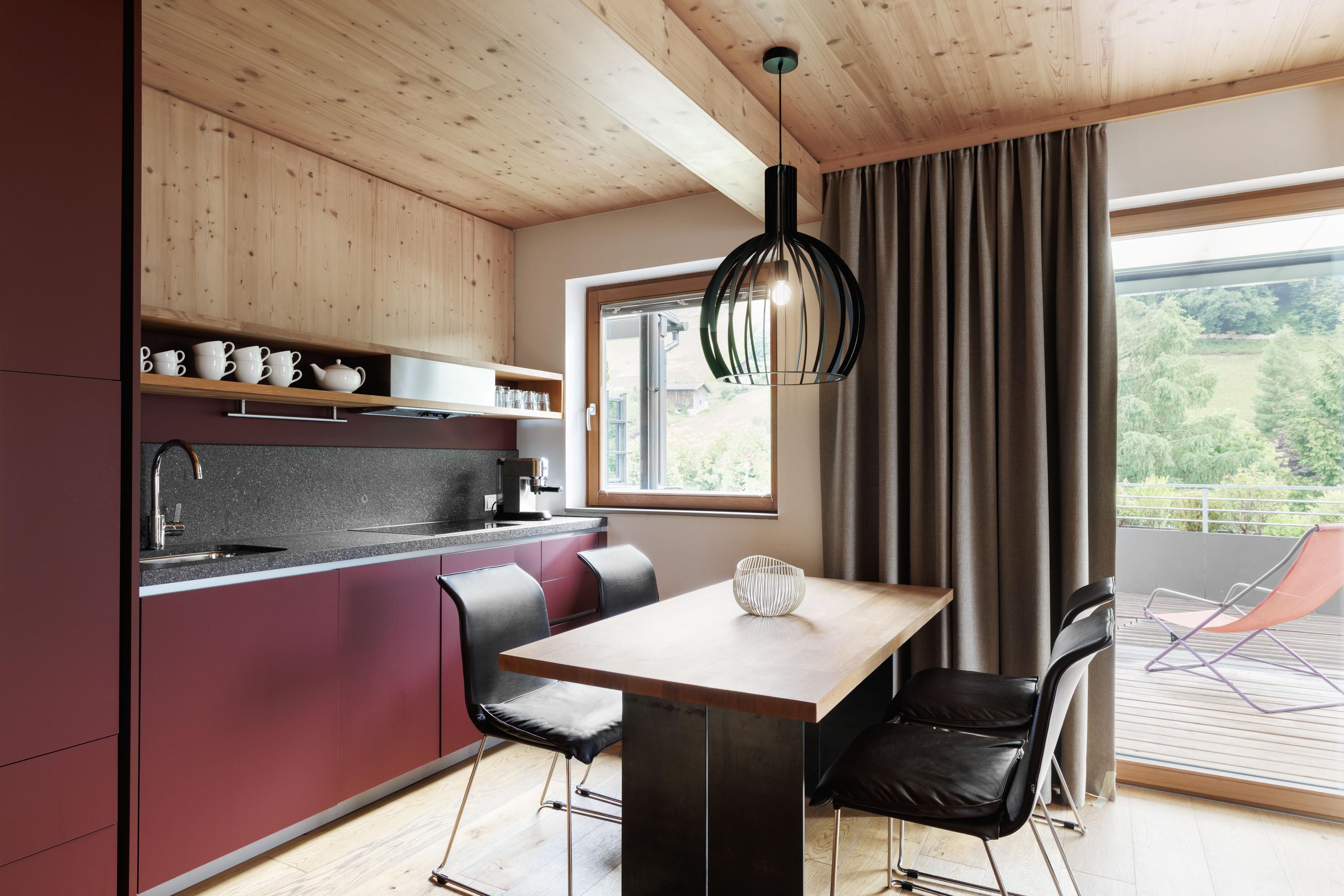 Eine moderne Küche mit Holzdetails und einem großen Fenster. Der Tisch ist aus Holz und die Stühle sind schwarz.