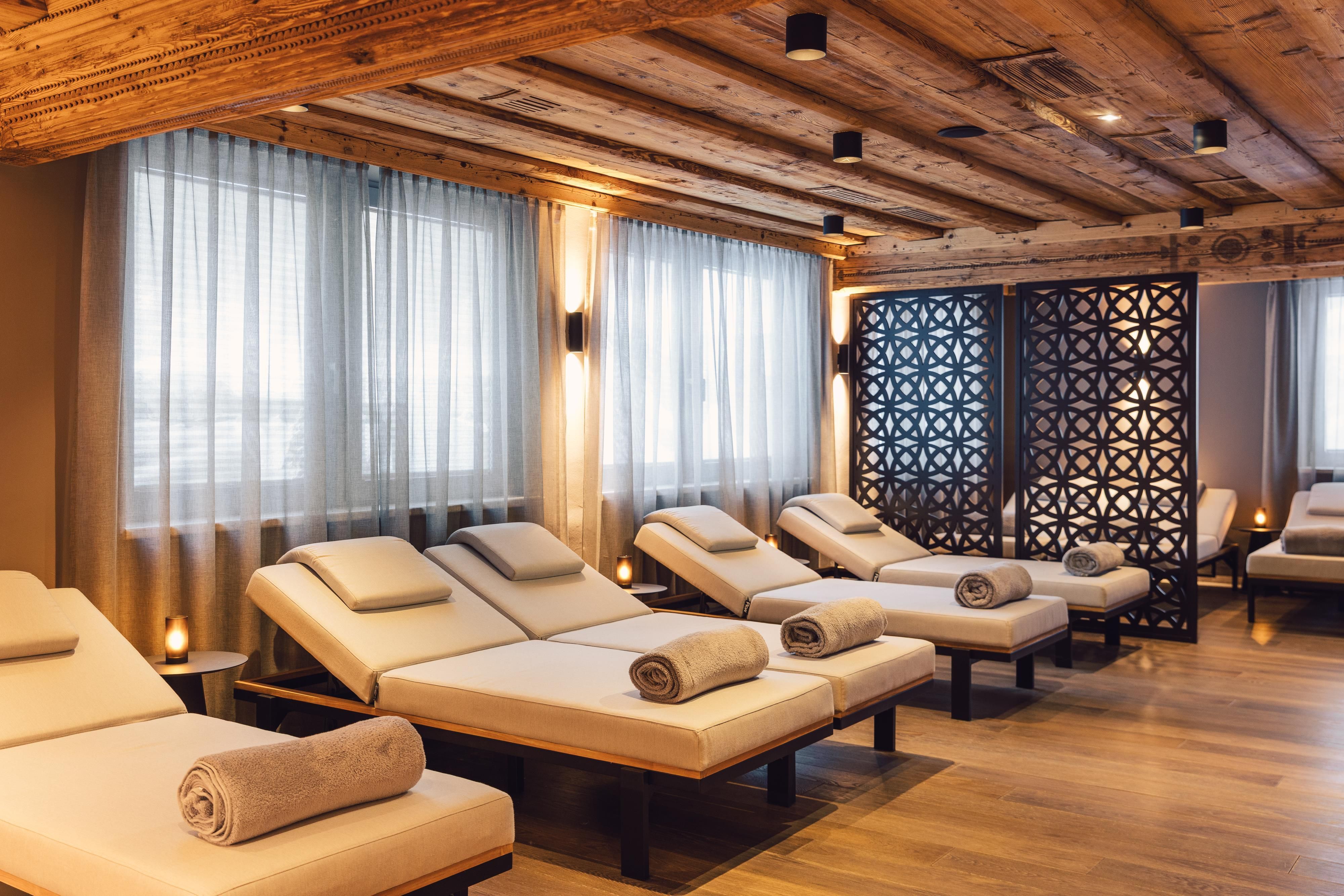Ein entspannender Wellnessbereich mit modernen Liegen und sanfter Beleuchtung. Die Holzdecke und die Vorhänge schaffen eine ruhige Atmosphäre.
