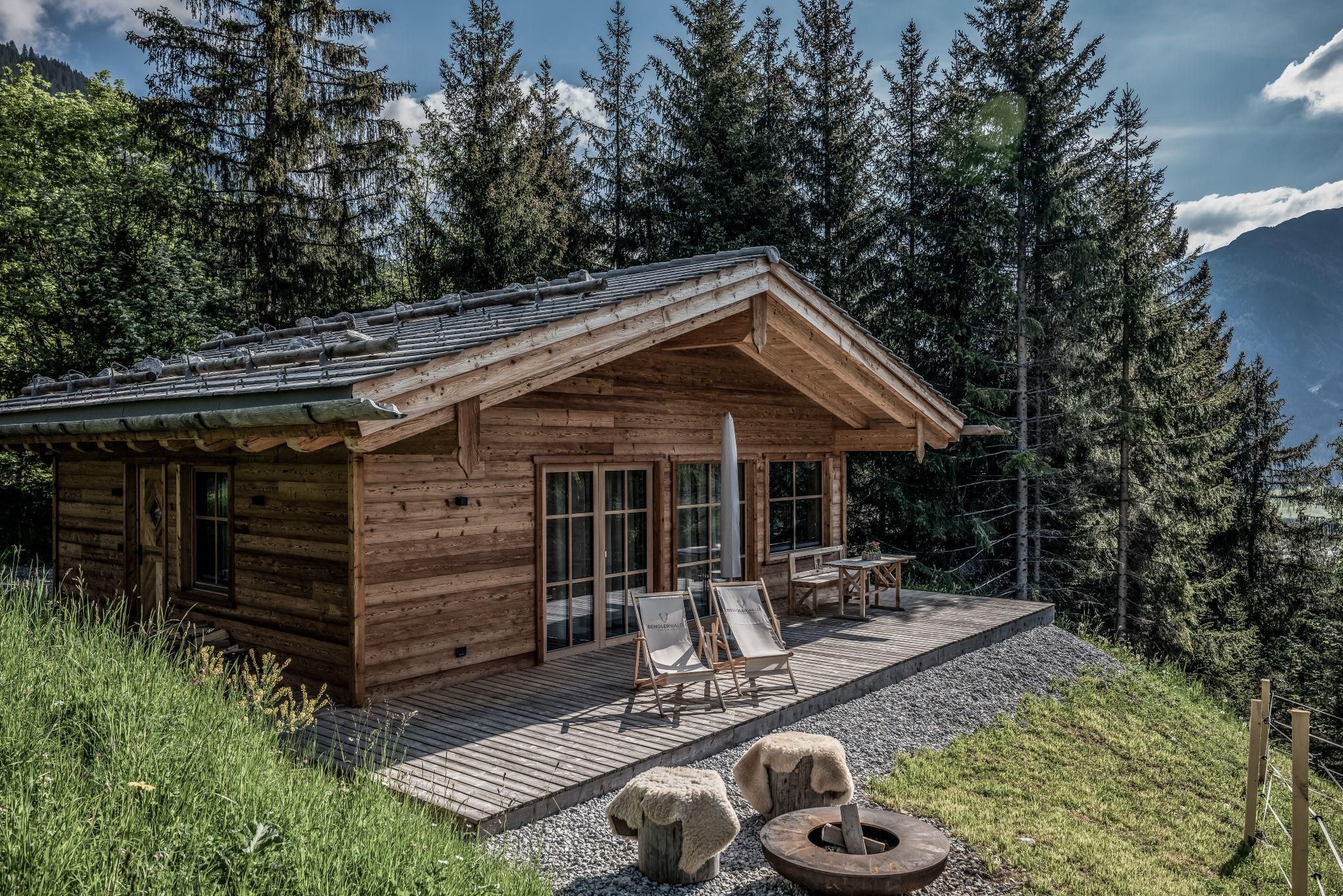 Ein gemütliches Chalet inmitten von Tannenbäumen. Die Veranda bietet Platz für Liegestühle und einen wunderschönen Ausblick auf die Natur.