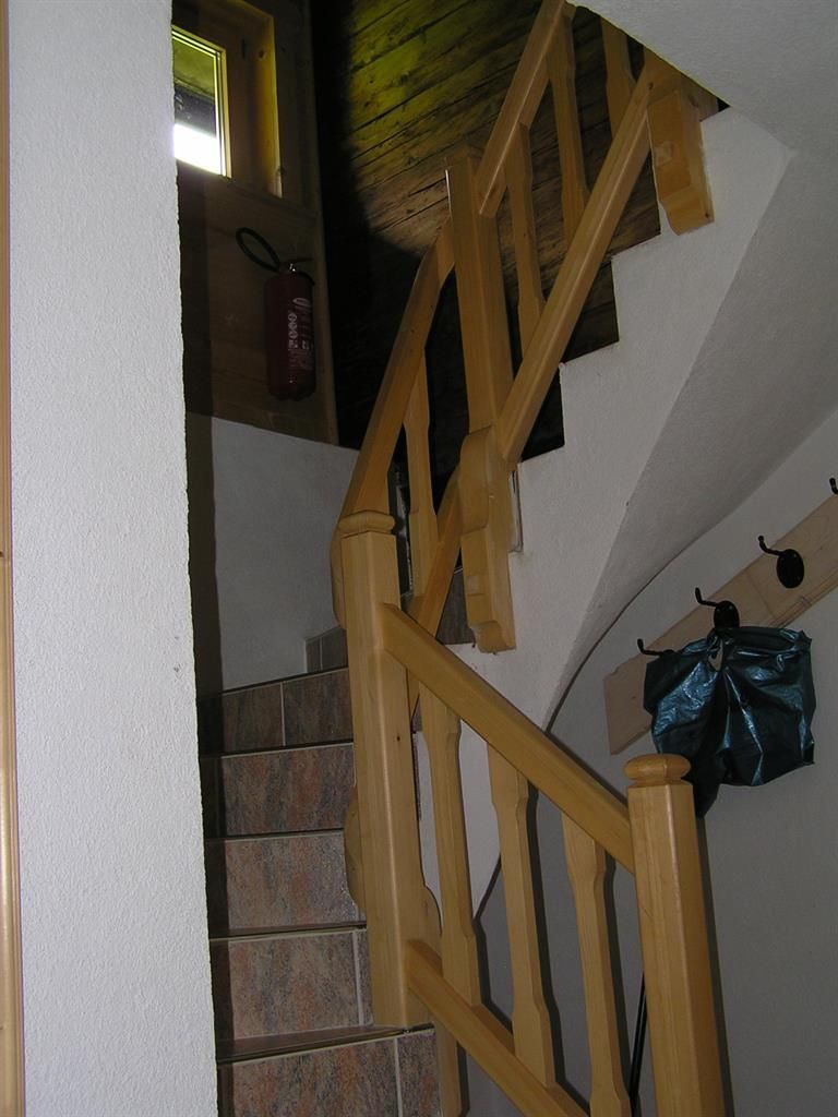 Eine Treppe mit einem Holzgeländer führt nach oben. Der Raum ist hell erleuchtet und hat eine gemütliche Atmosphäre.