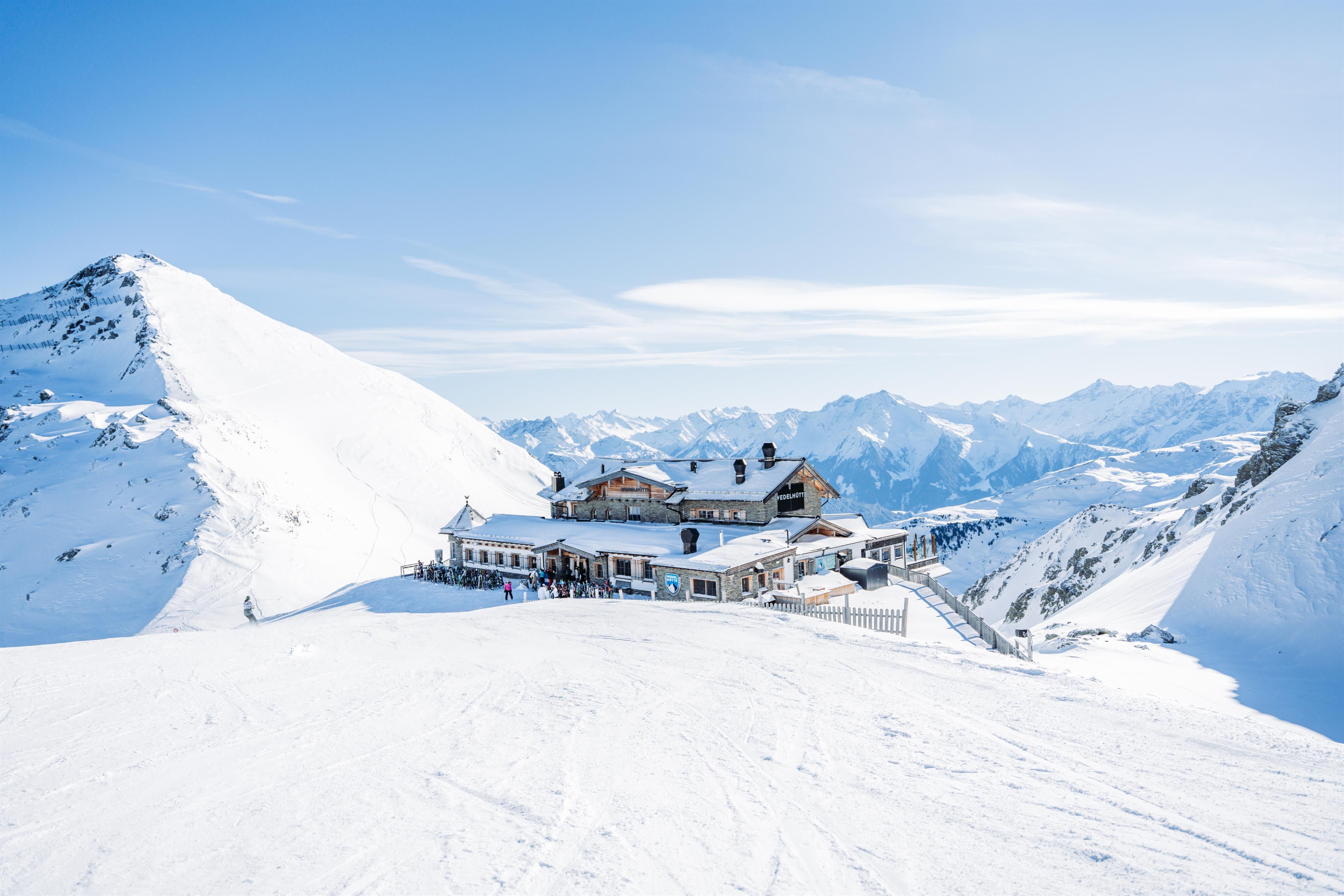 Ein Bergrestaurant in den Alpen, umgeben von schneebedeckten Gipfeln. Der Himmel ist klar und strahlend blau.