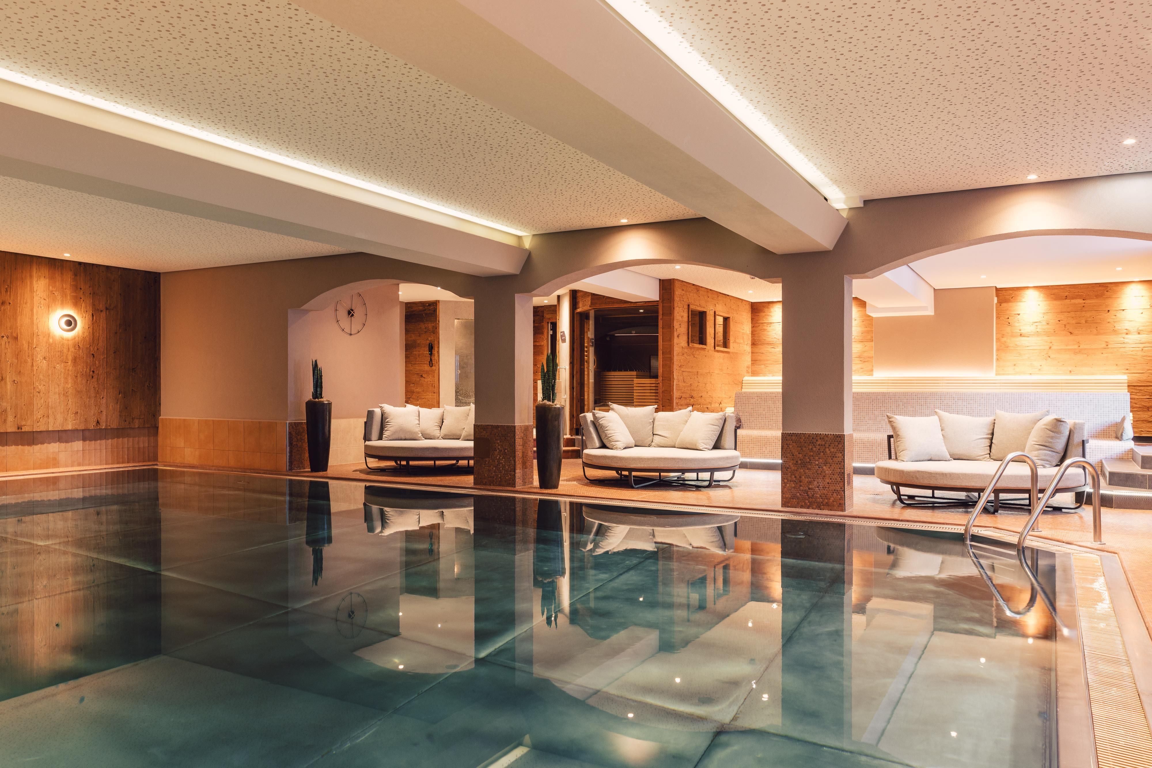 Ein eleganter Innenpool in einem stilvollen Wellnessbereich. Entspannte Sitzgelegenheiten und warmes Licht schaffen eine einladende Atmosphäre.