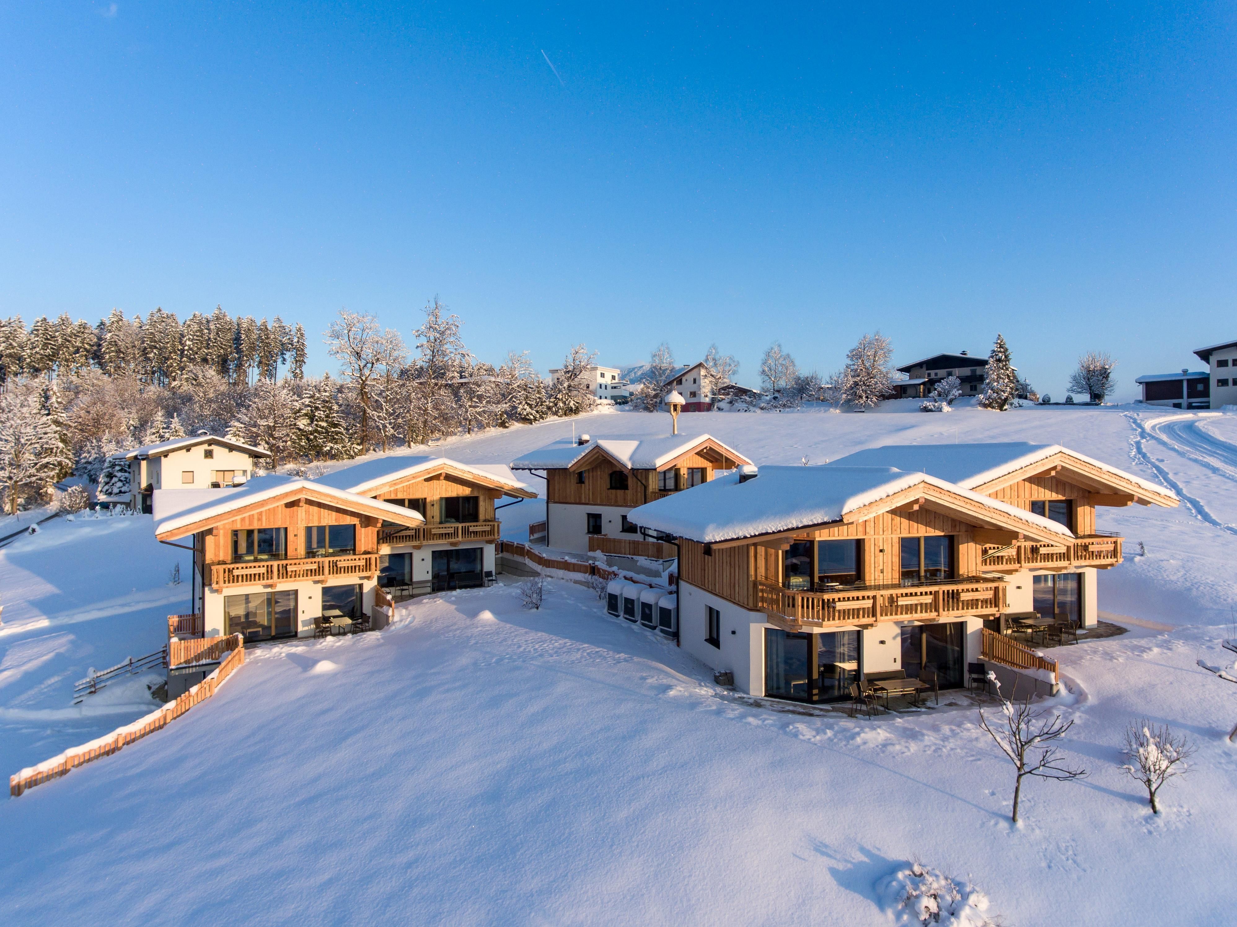 Eine malerische alpine Landschaft mit schneebedeckten Hügeln und traditionellen Holzchalets. Der klare blaue Himmel schafft eine ruhige Winteratmosphäre.