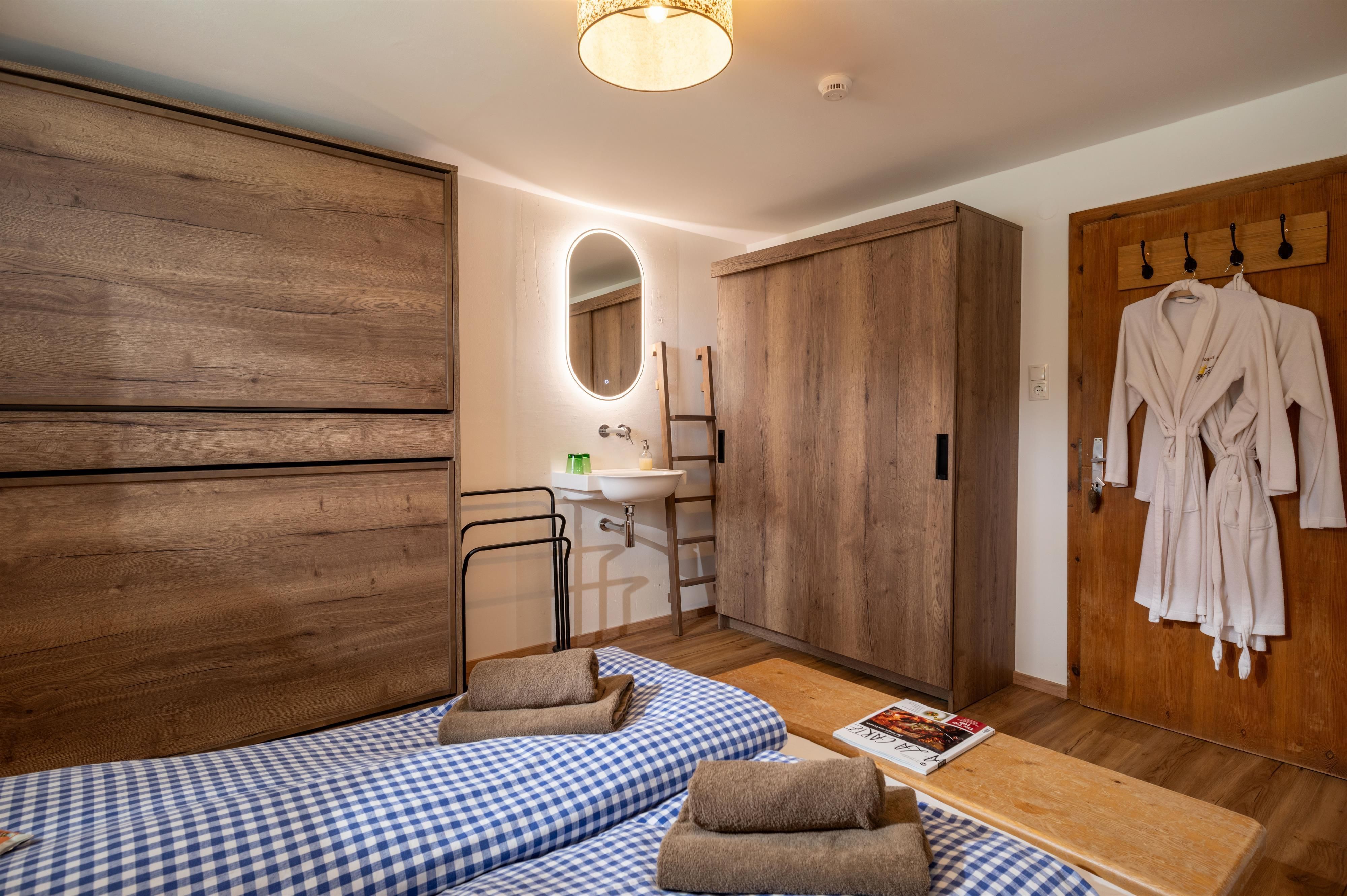 Ein gemütliches Zimmer mit Holzmöbeln und einem großen Fenster. Auf dem Boden liegen Decken und Handtücher sind bereit zum Gebrauch.