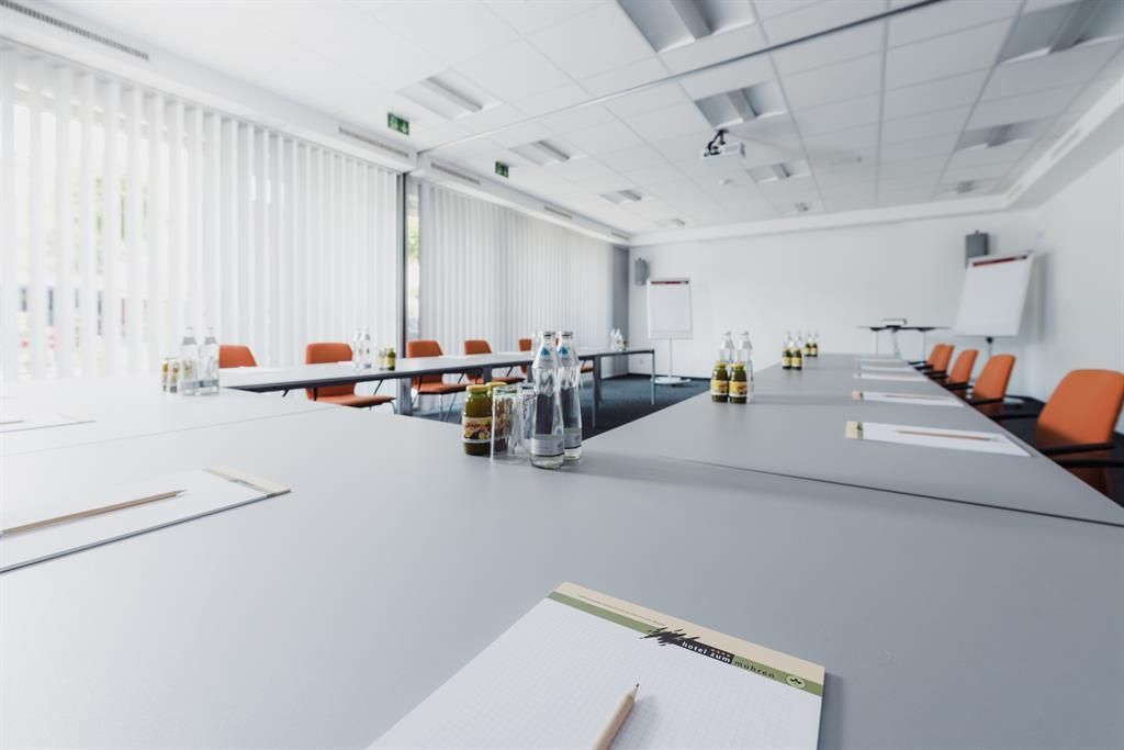 Ein modernes Besprechungszimmer mit orangefarbenen Stühlen und eleganten Tischen. Auf den Tischen stehen Wasserflaschen und Notizblöcke.