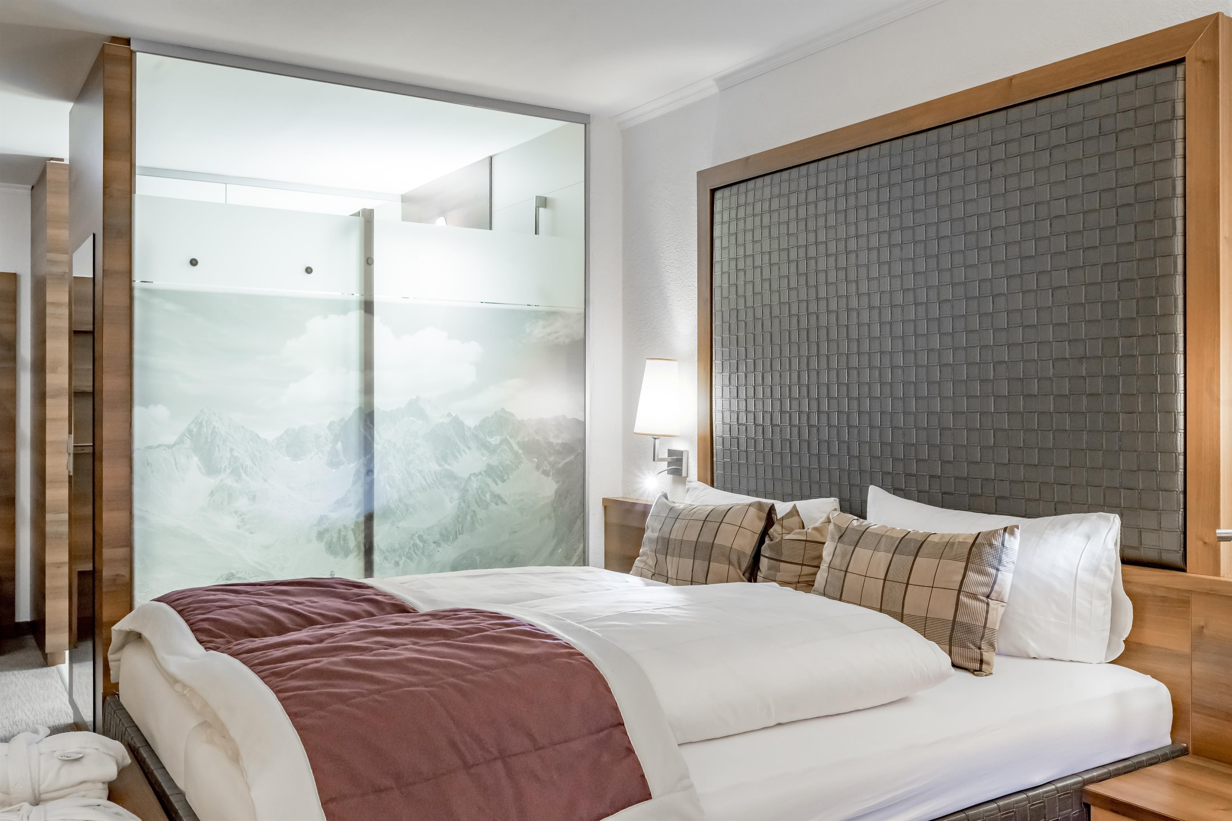 Ein modernes Schlafzimmer mit einem großen Bett und eleganter Dekoration. Eine Glaswand zeigt eine malerische Berglandschaft.