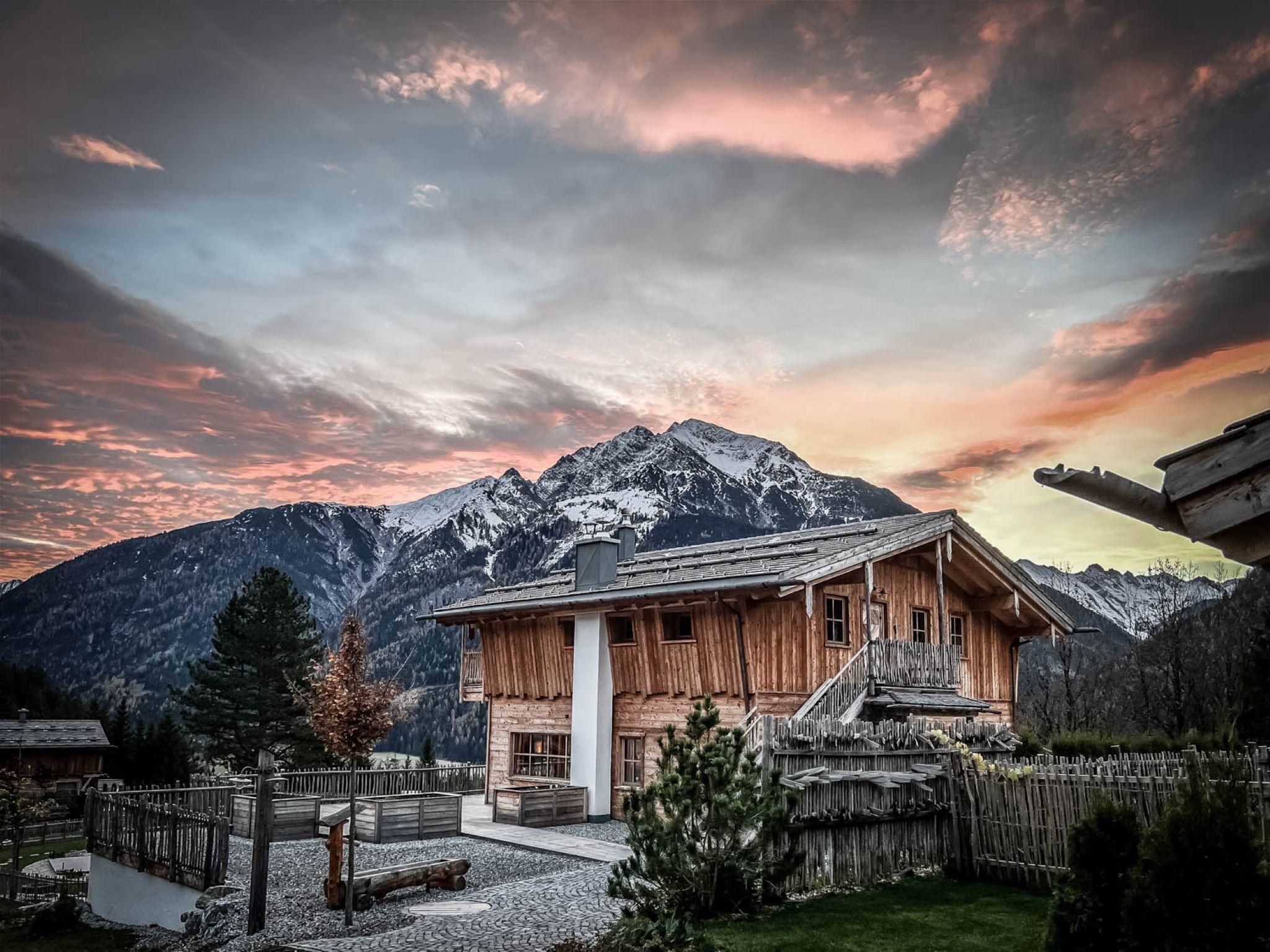 Ein charmantes Chalet vor majestätischen Bergen. Der Himmel leuchtet in warmen Farben während des Sonnenuntergangs.