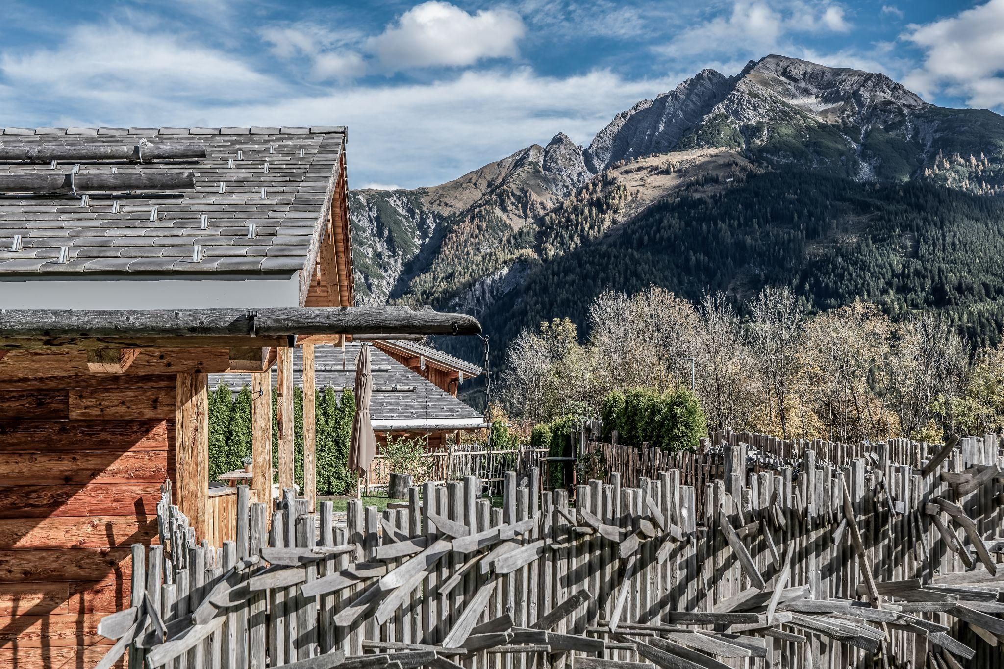 Ein malerisches Bergpanorama mit hohen Gipfeln und grünen Wäldern. Im Vordergrund sind Chalets und Zäune zu sehen.