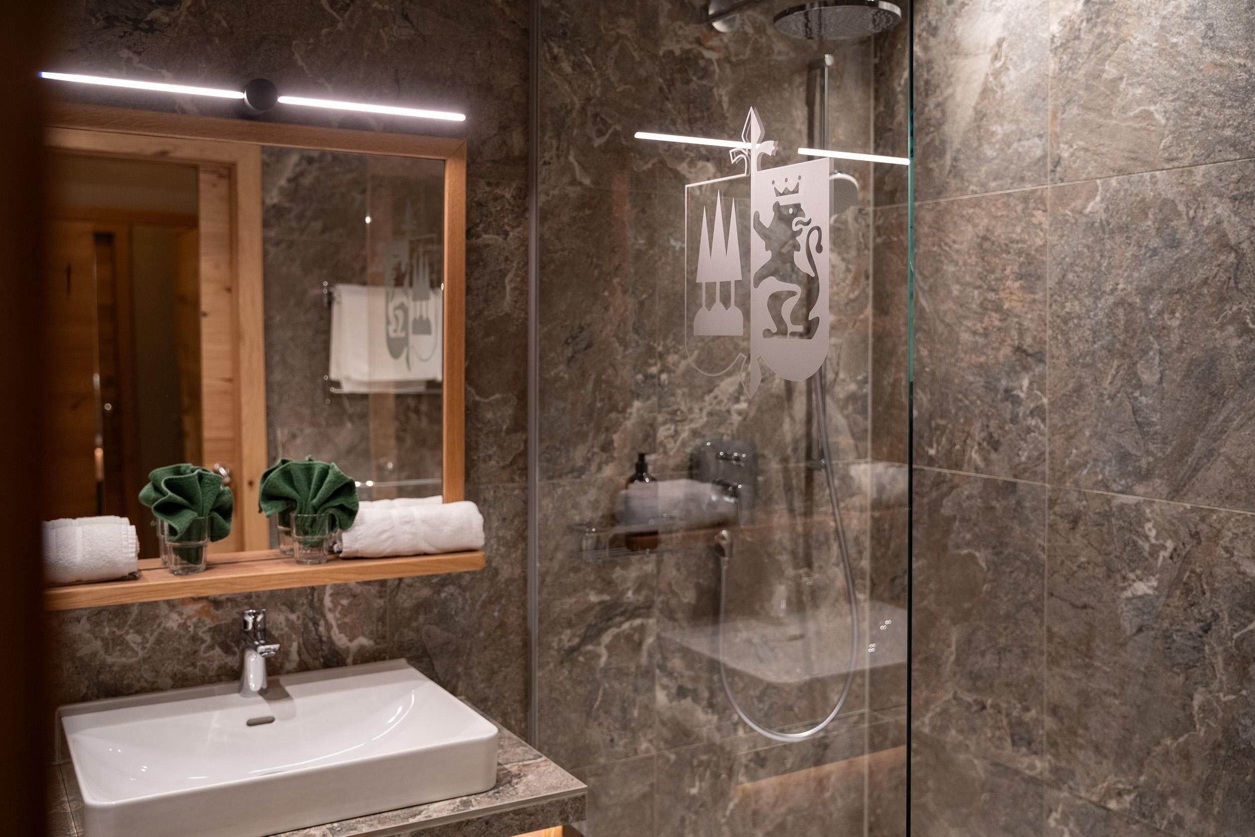 Ein modernes Bad mit eleganten Marmorwänden und einer begehbaren Dusche. Auf der Anrichte sind gepflegte Handtücher und dekorative Pflanzen platziert.