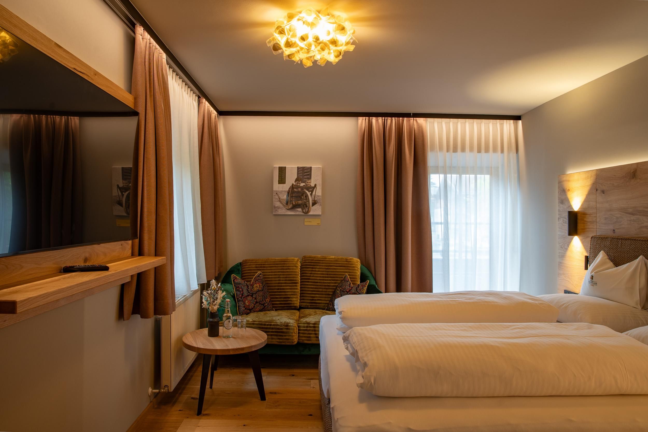 Ein modernes Zimmer mit zwei Betten und einem gemütlichen Sofa. Große Fenster lassen viel Licht herein und sorgen für eine einladende Atmosphäre.