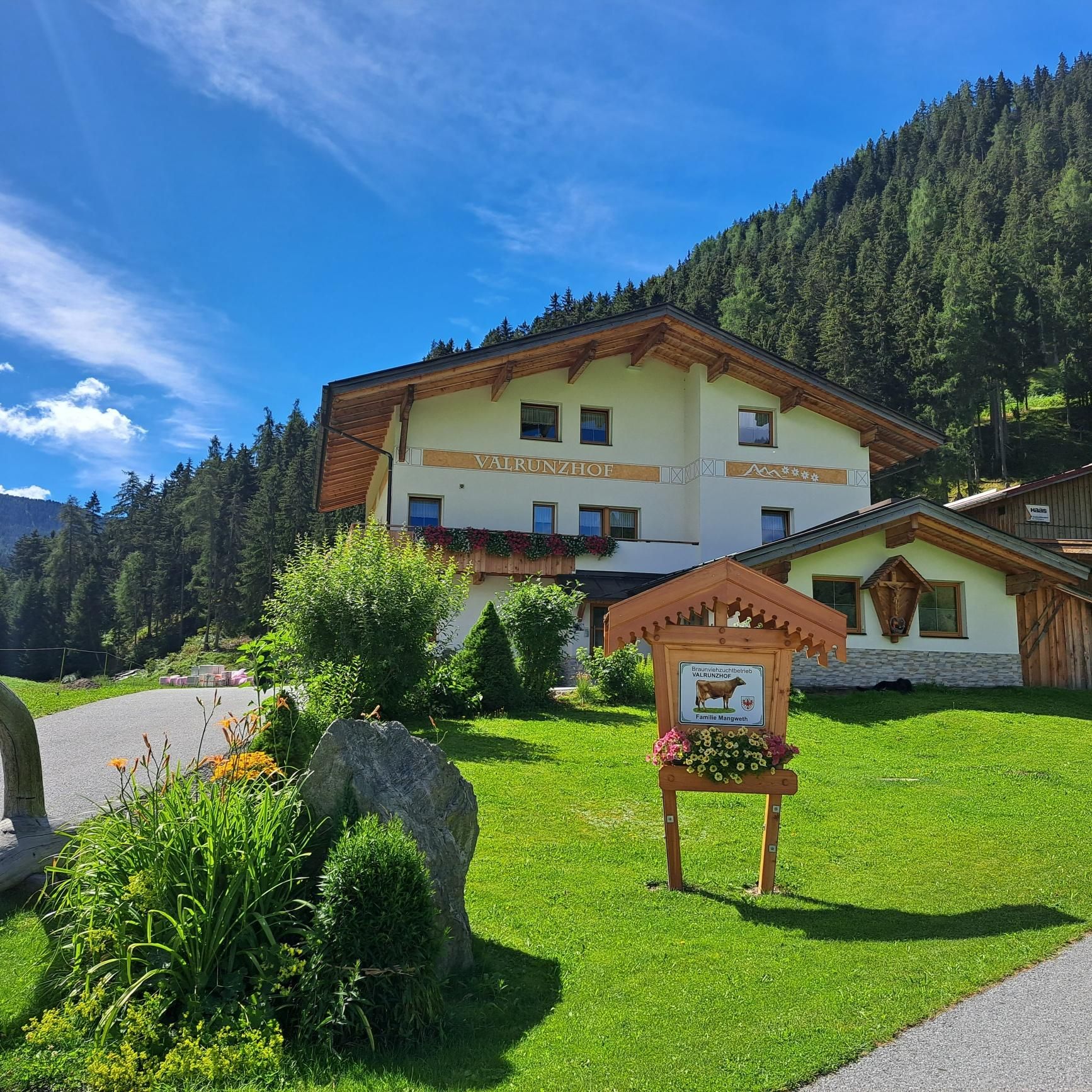 Ein typisches alpenländisches Haus umgeben von grüner Wiese und Wald.