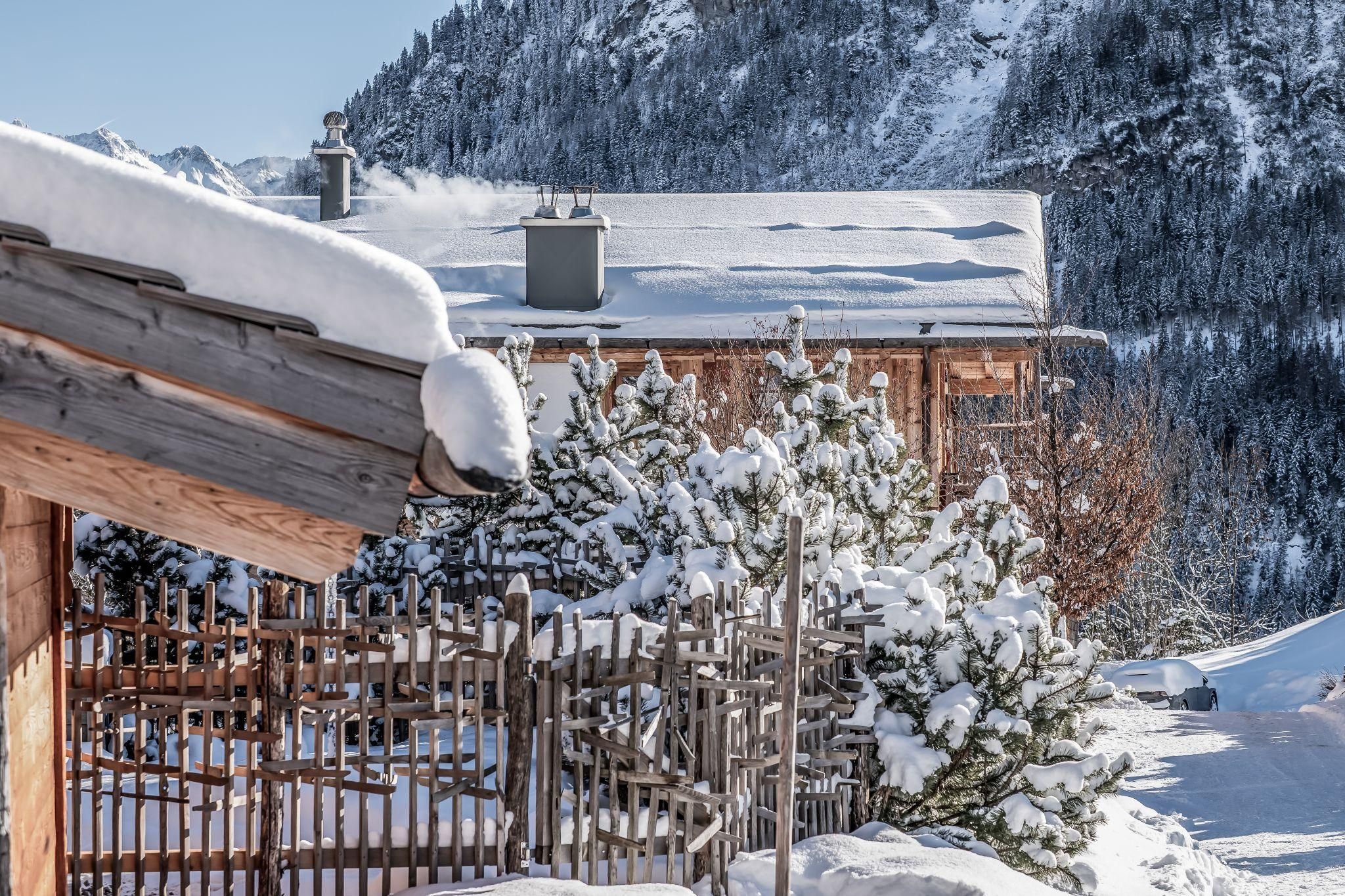Eine winterliche Landschaft mit schneebedeckten Chalets und Tannenbäumen. Im Hintergrund sind verschneite Berge sichtbar.