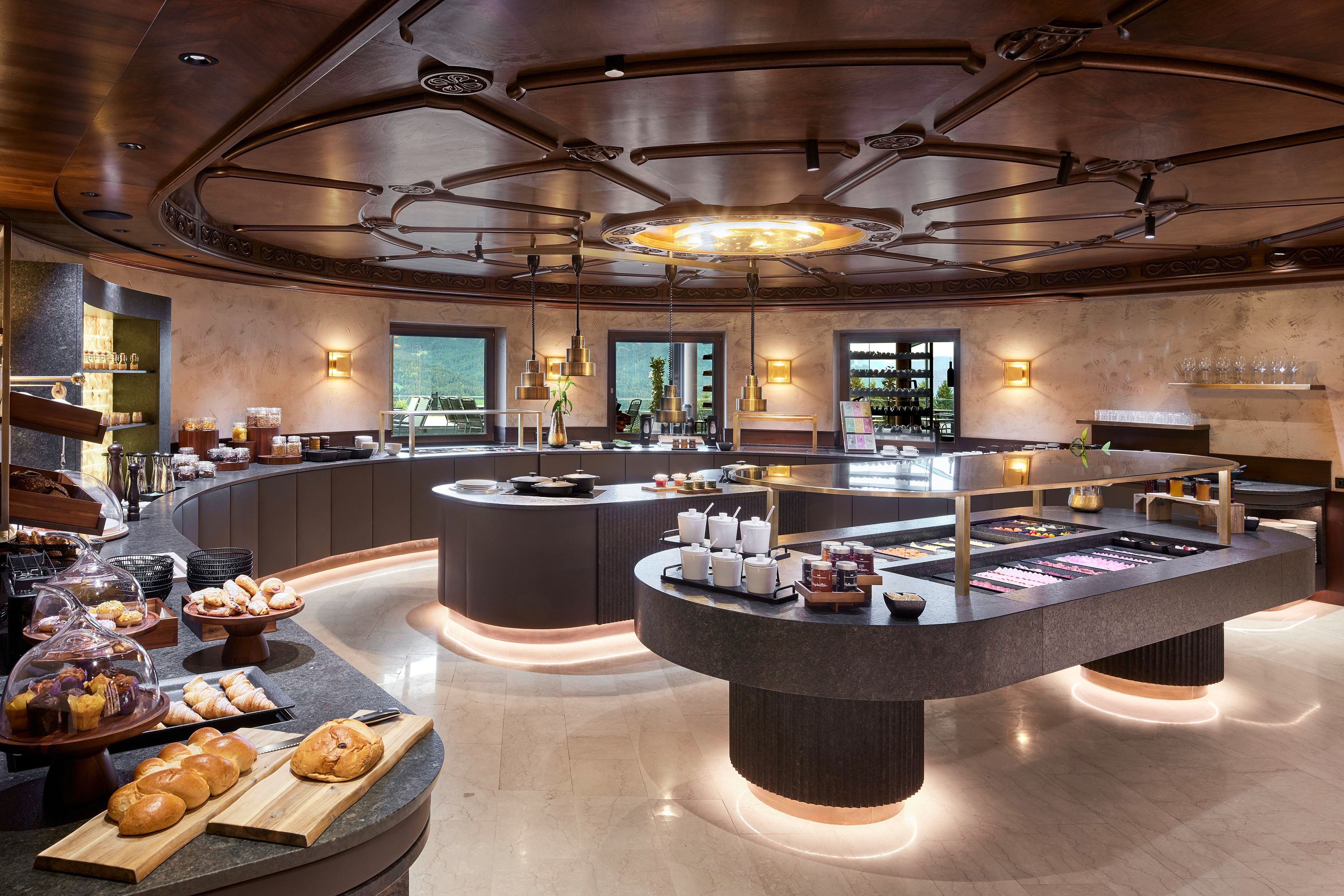 Ein eleganter Speisesaal mit einem runden Buffet und ansprechender Beleuchtung. Auf den Tischen sind frisches Gebäck und verschiedene Speisen angerichtet.