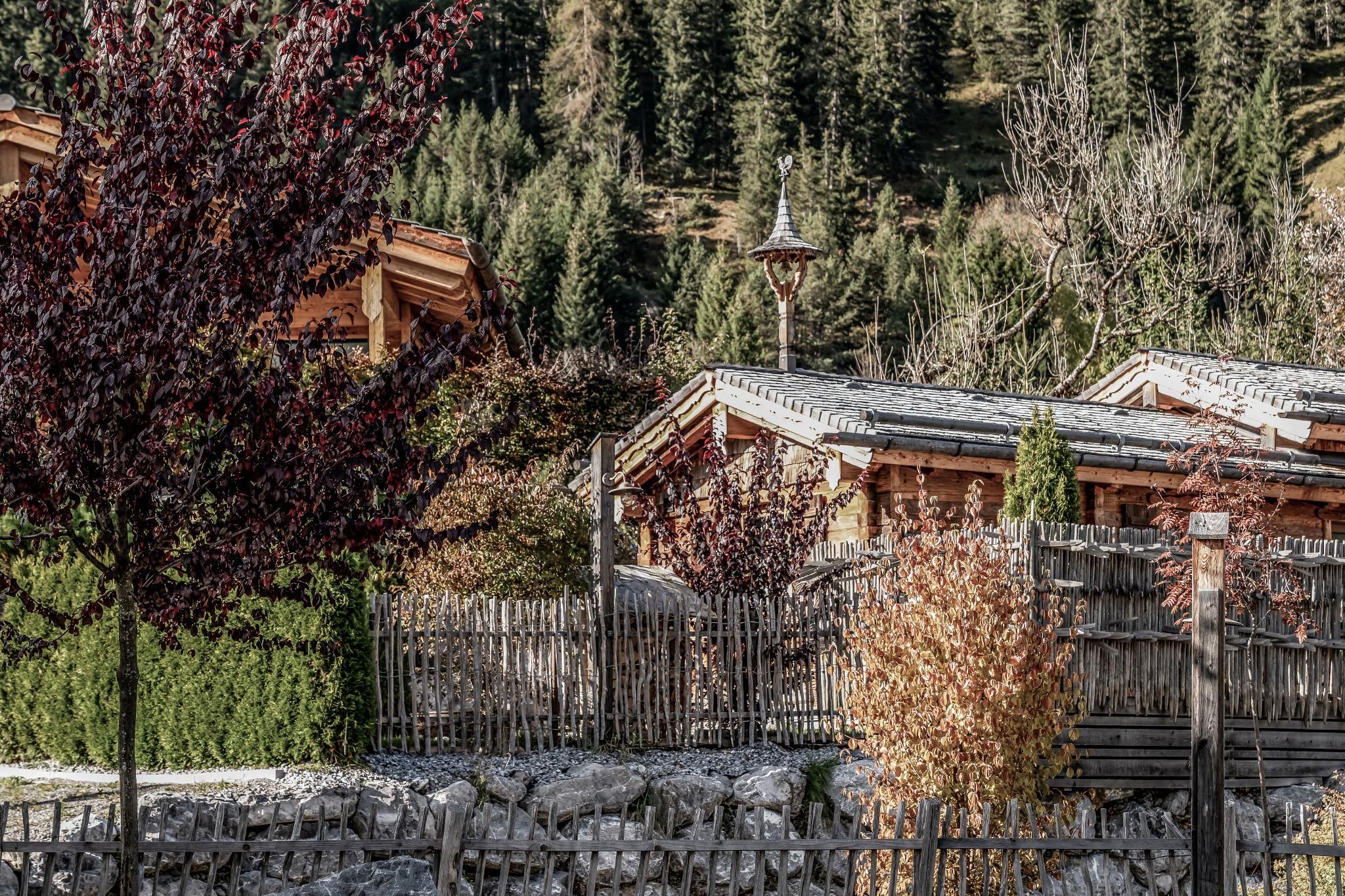 Eine idyllische Landschaft mit traditionellen Holzchalets und bunten Bäumen. Im Hintergrund sind sanfte Hügel und dichter Wald zu sehen.