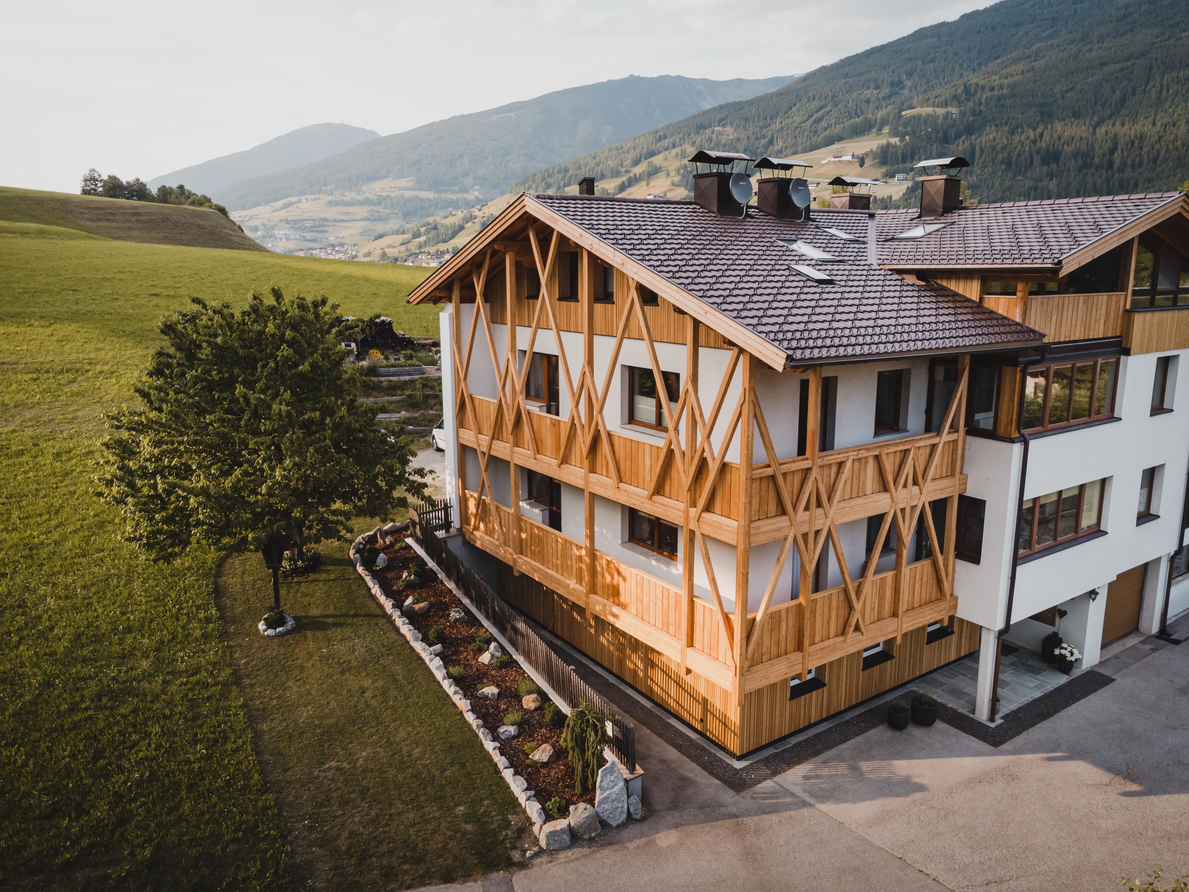 Ein modernes Holzhaus in einer malerischen Landschaft mit grünen Wiesen und sanften Hügeln. Die Architektur kombiniert traditionelles und modernes Design.