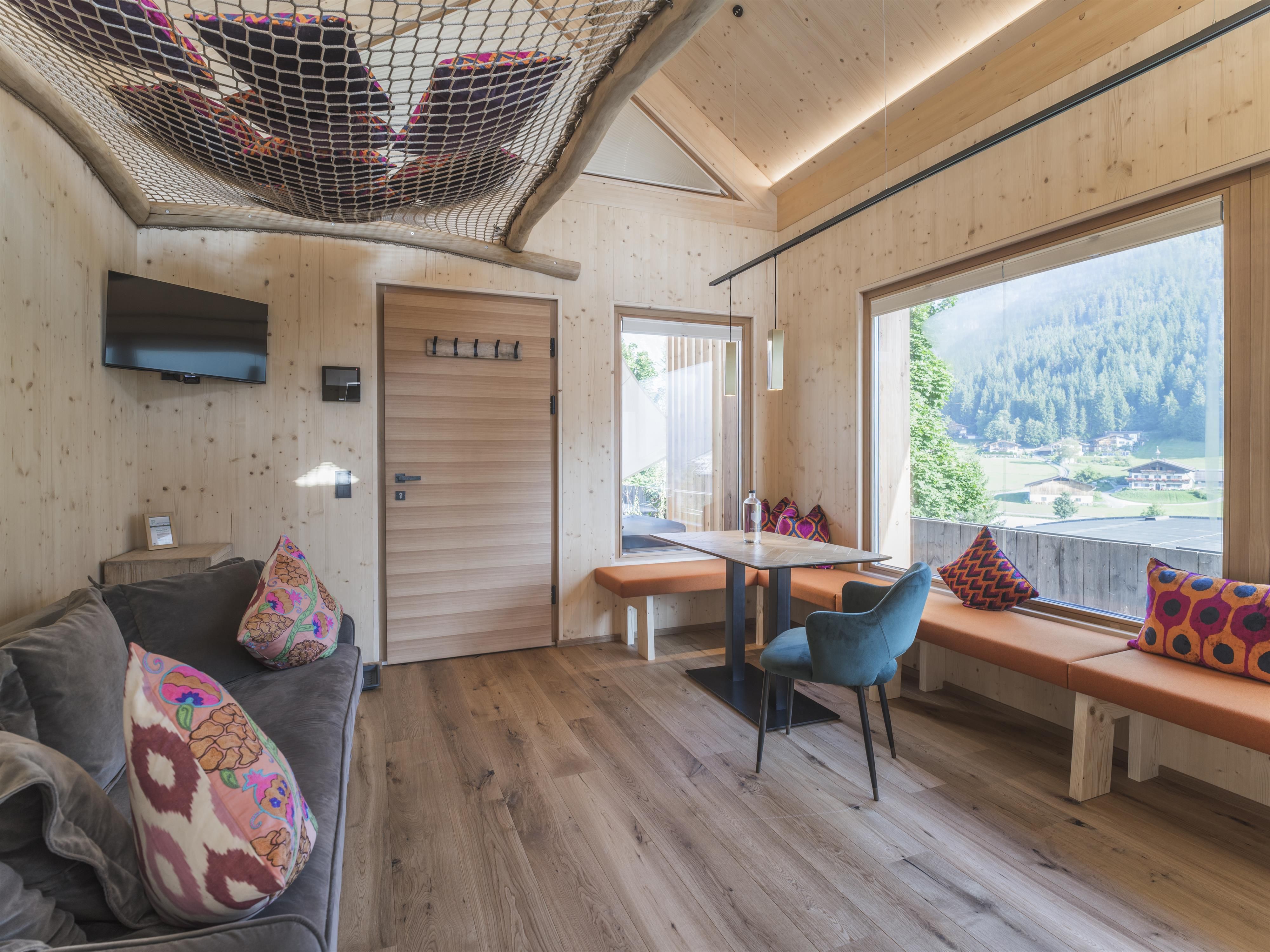 Ein modernes, gemütliches Wohnzimmer mit Holzverkleidung und großen Fenstern. Es gibt einen Sofa, einen Tisch und eine schöne Aussicht auf die Natur.