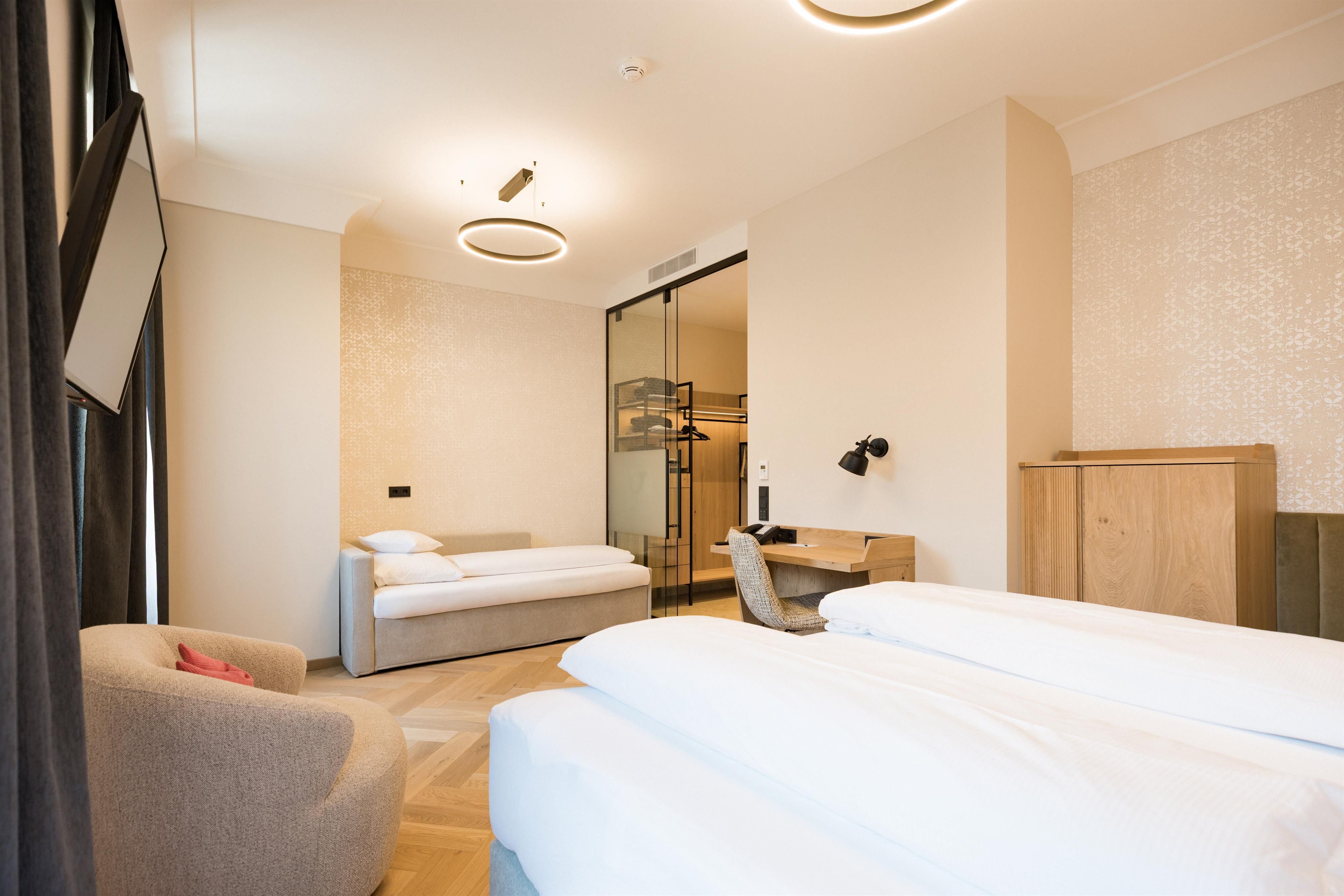 Ein modernes Hotelzimmer mit zwei Betten und einem gemütlichen Stuhl. Die Wände sind in neutralen Tönen gehalten und das Zimmer wirkt hell und einladend.