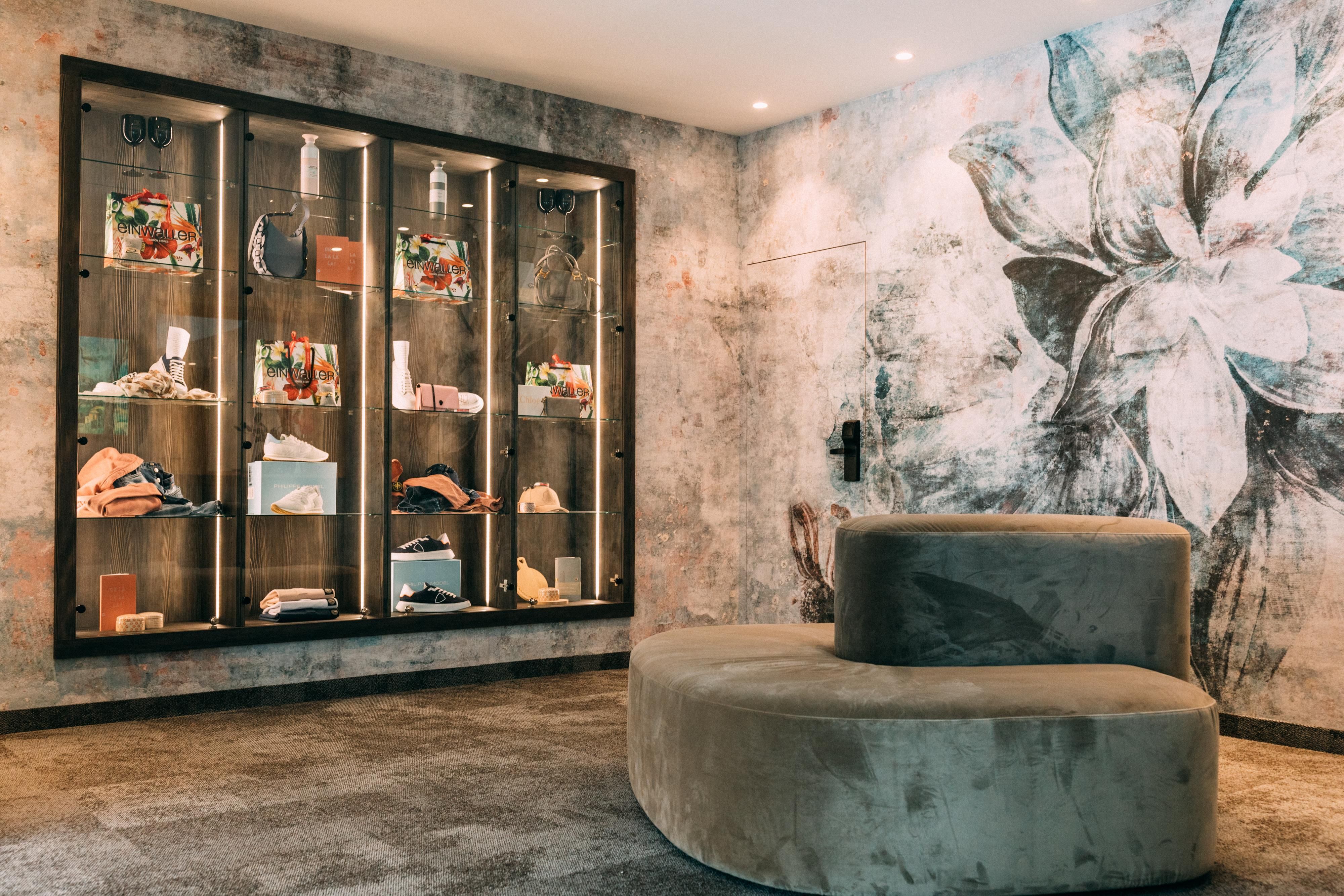 Ein stilvolles Interieur mit einer runden Sitzgelegenheit und einer Glasvitrine. Die Wand ist mit einem floralen Motiv dekoriert, während die Vitrine verschiedene Accessoires zeigt.