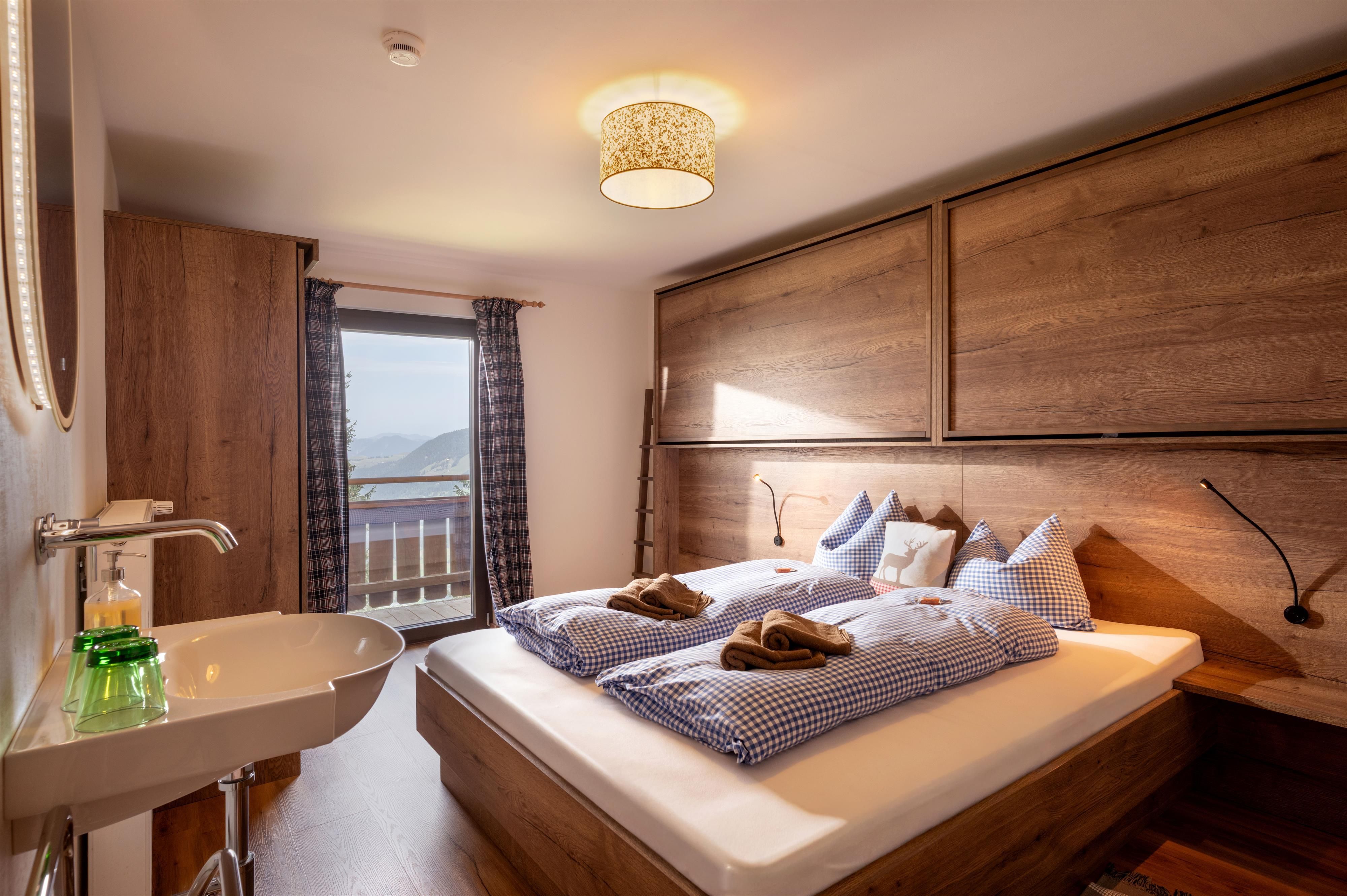 Ein gemütliches Schlafzimmer mit einem Doppelbett und Holzvertäfelungen. Große Fenster bieten einen Blick nach draußen und viel Tageslicht.