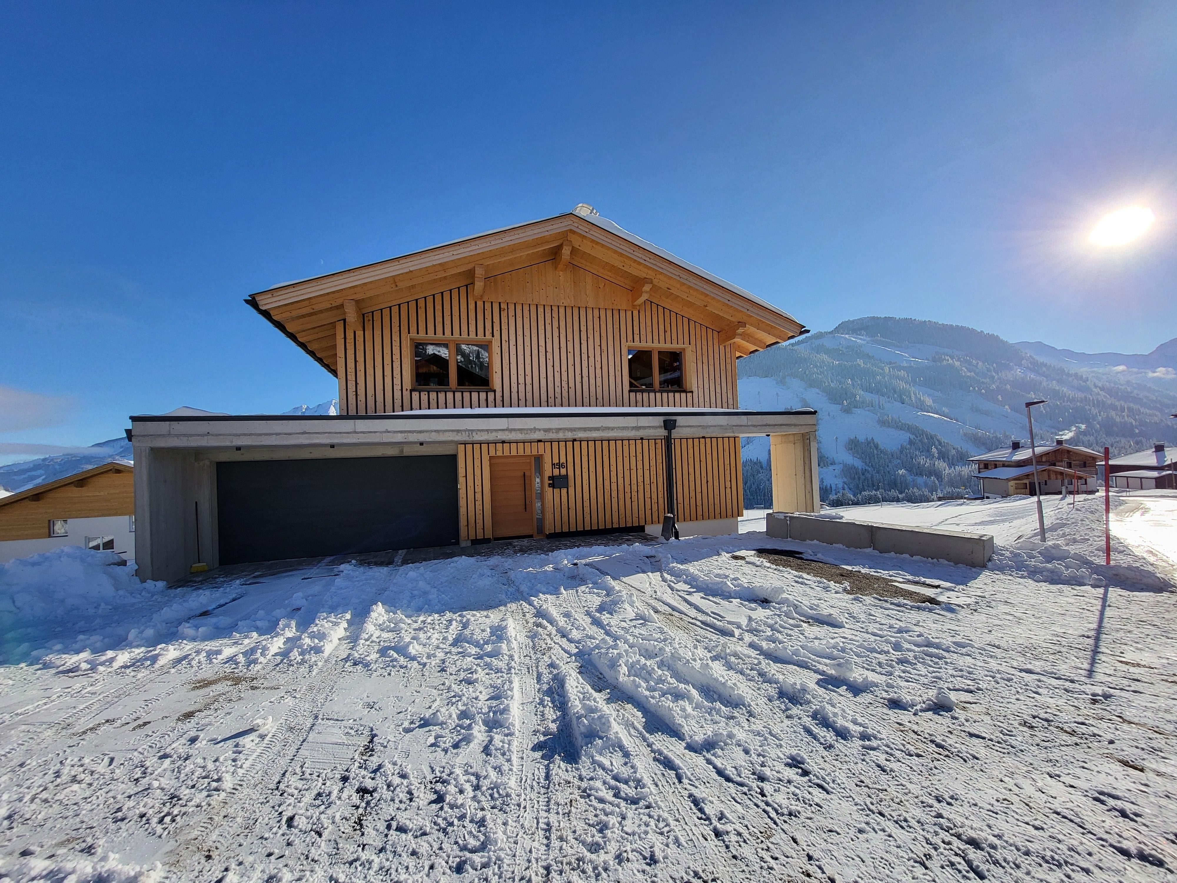 Ein modernes Holzhaus im Schnee mit einer schönen Berglandschaft im Hintergrund. Der Himmel ist klar und sonnig.