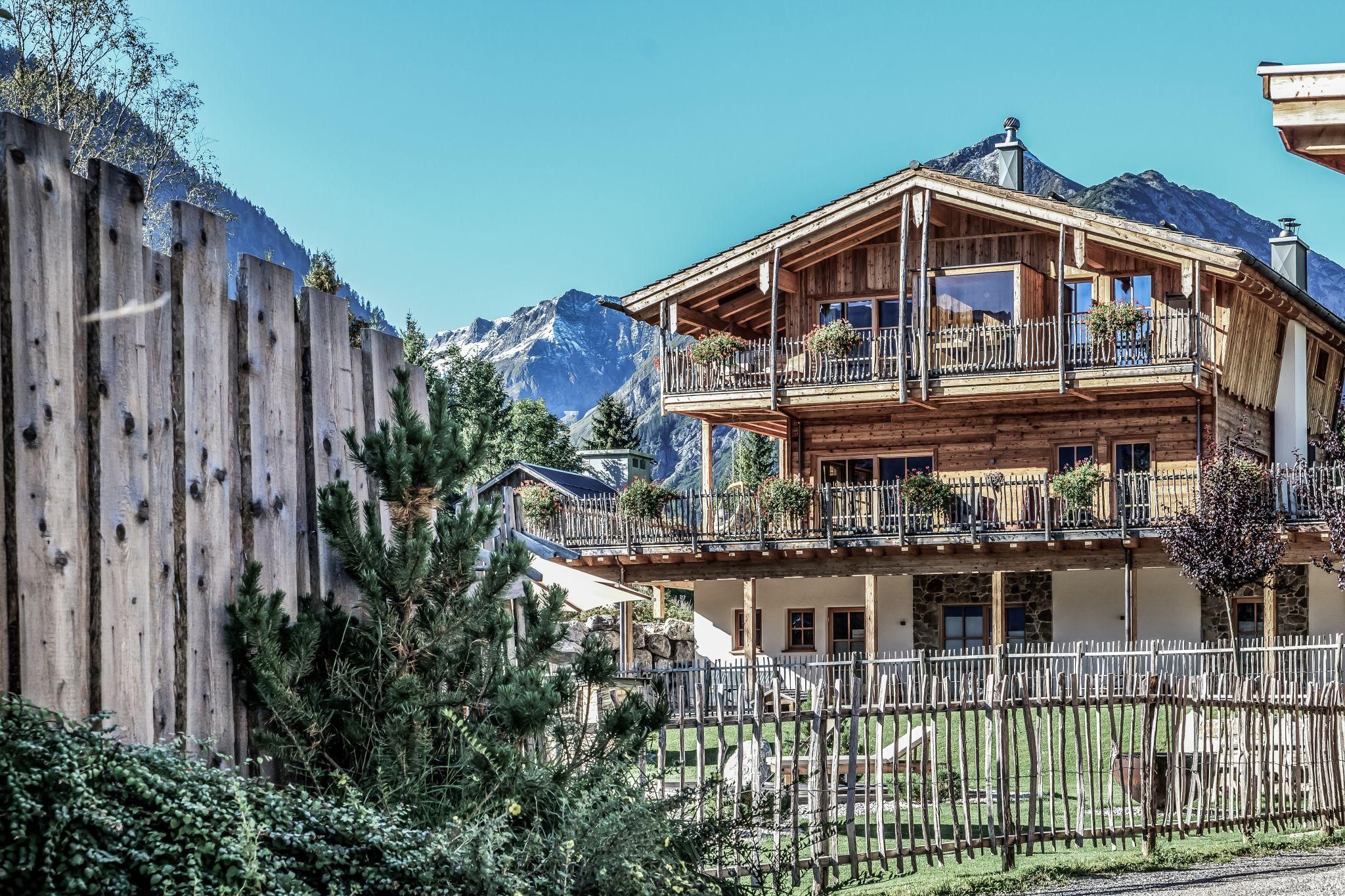 Ein charmantes Chalet in den Bergen mit Balkonen und einer schönen Aussicht. Im Vordergrund sieht man einen Zaun und grünes Gras.