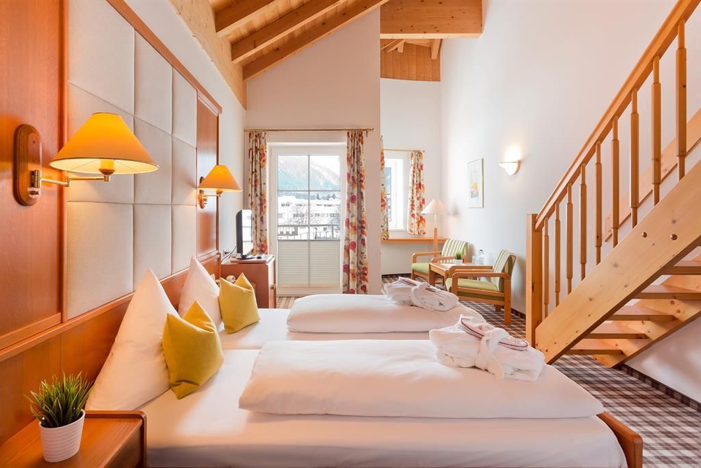 Ein gemütliches Hotelzimmer mit zwei Einzelbetten und modernen Möbeln. Große Fenster bieten einen Blick auf die Natur und viel Tageslicht.