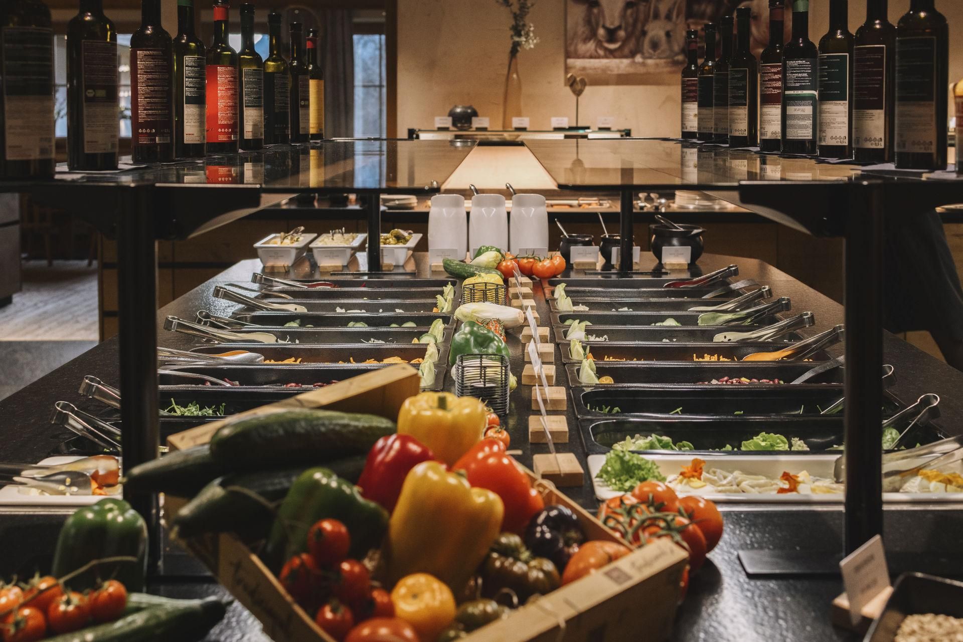 Eine bunte Auswahl an frischem Gemüse und Salat in einem Buffetbereich. Im Hintergrund stehen Flaschen mit verschiedenen Ölen und Essigen.