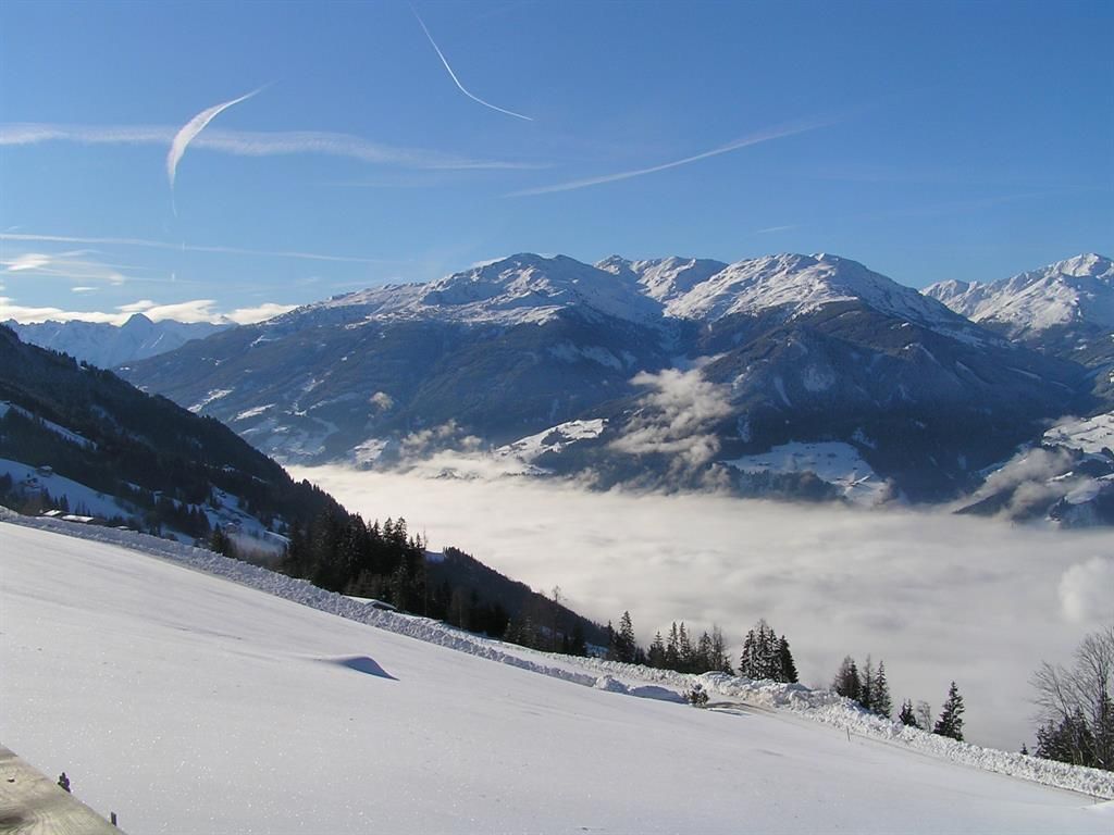Eine wunderschöne Berglandschaft mit schneebedeckten Gipfeln und einem klaren blauen Himmel. Im Tal liegen dichte Wolken.