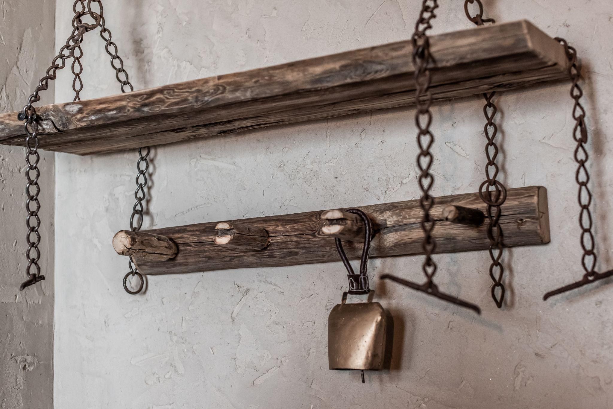 Ein rustikales Regal aus Holz mit Ketten hängt an der Wand. Darunter befindet sich eine kleine Glocke und einige Holzklötze.
